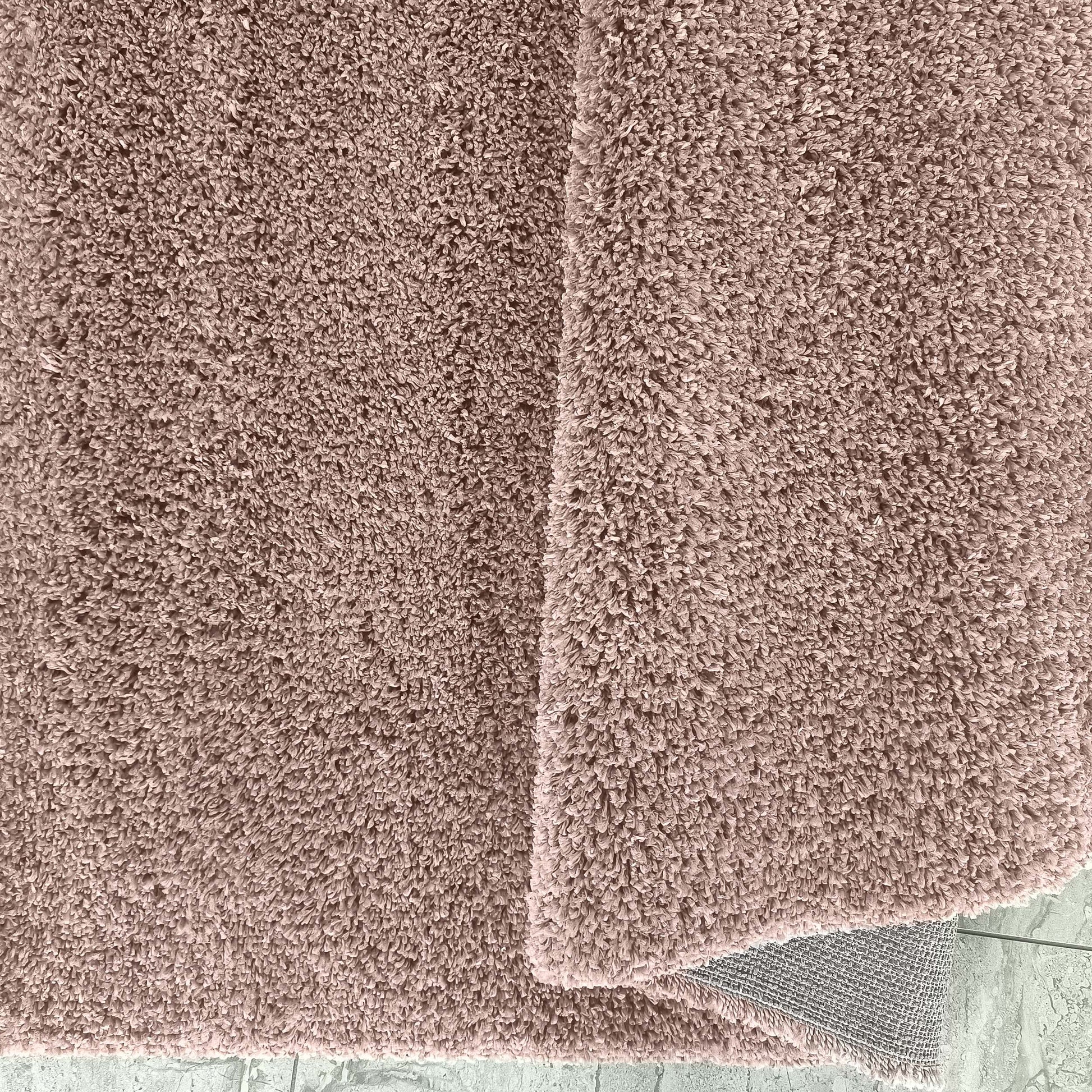 Tapis à poils longs rose poudré et moelleux, plié pour révéler son envers gris tissé sur un sol clair