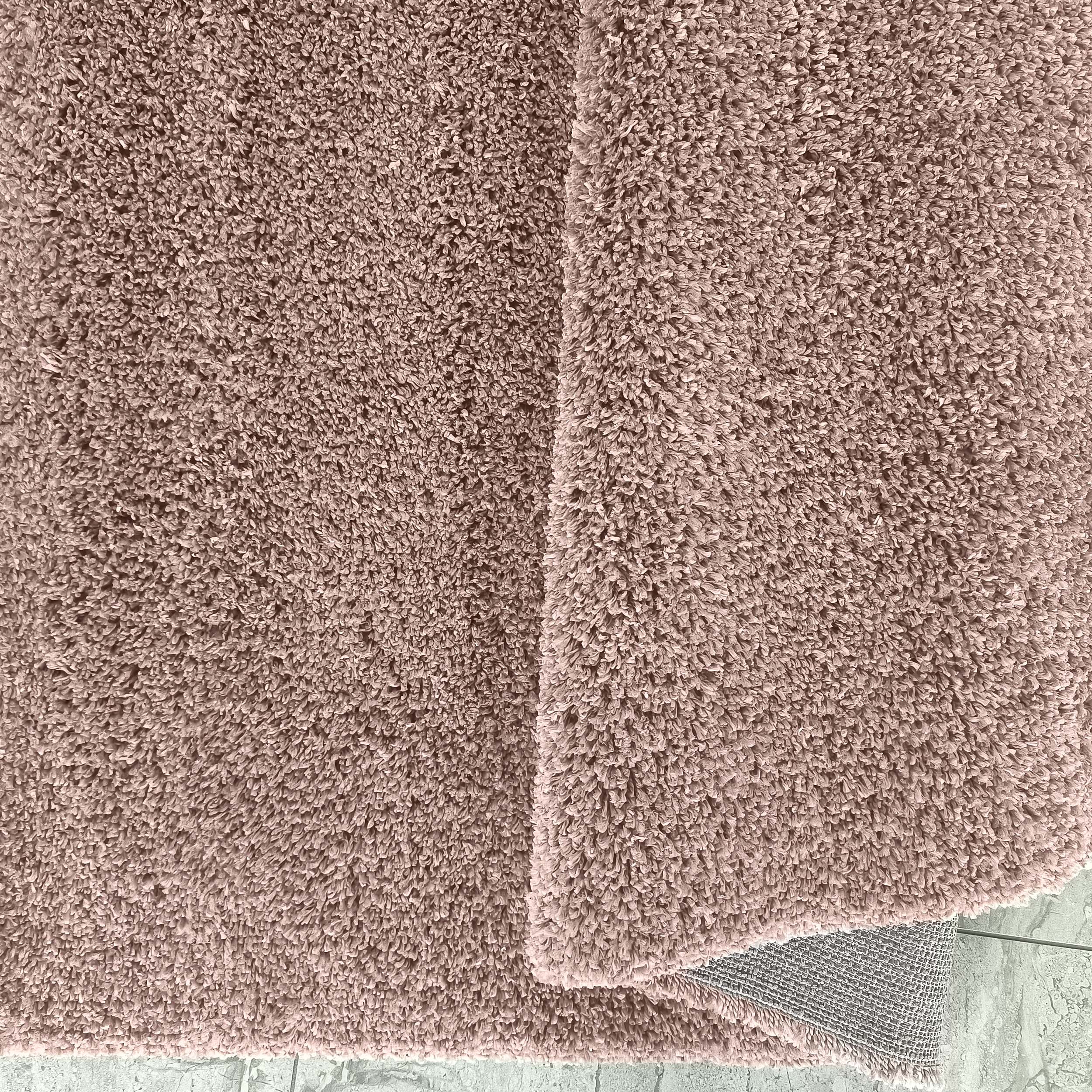 Tapis à poils longs rose poudré et moelleux, plié pour révéler son envers gris tissé sur un sol clair