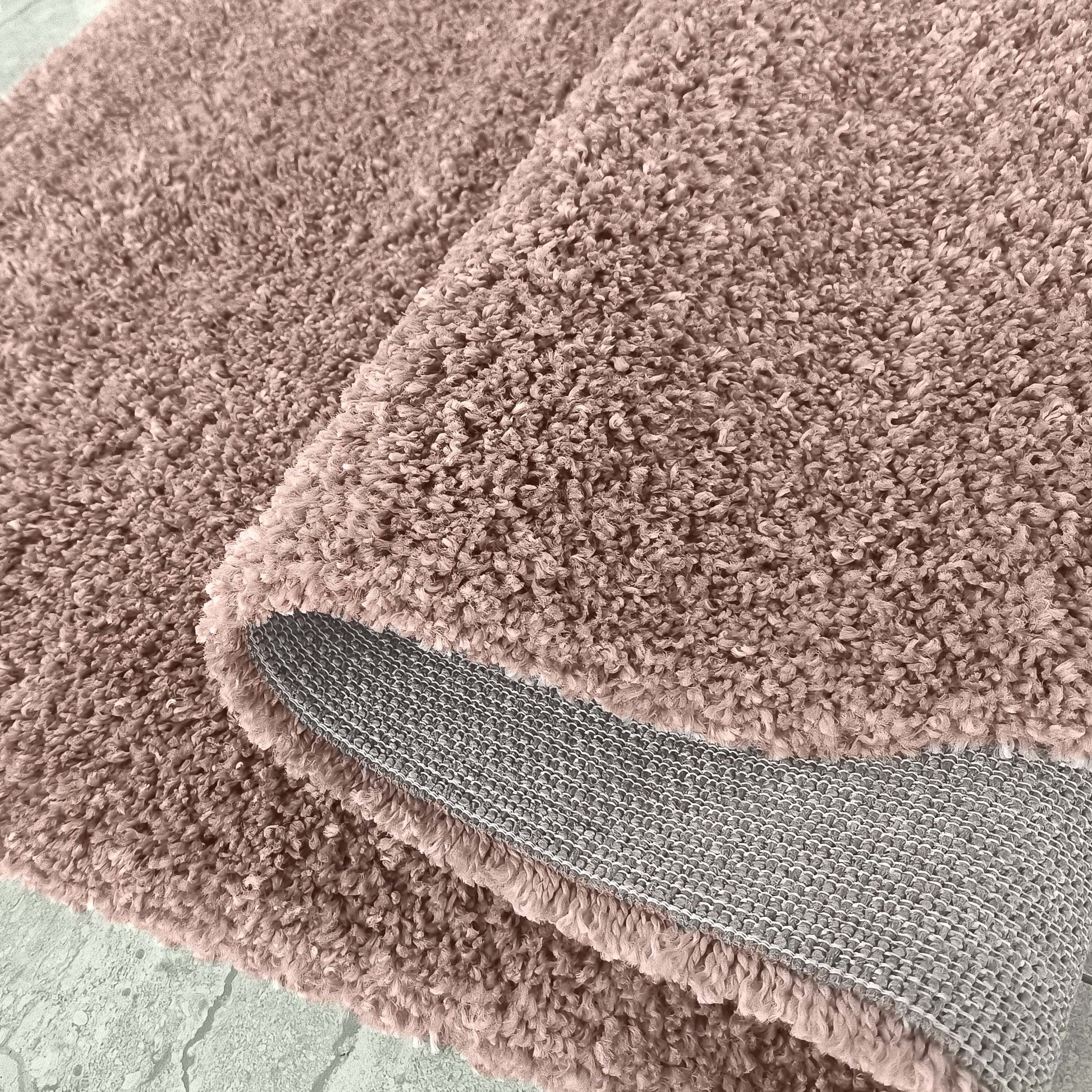 Tapis épais couleur beige rosé avec une texture moelleuse de longs poils bouclés, dont le revers gris est visible