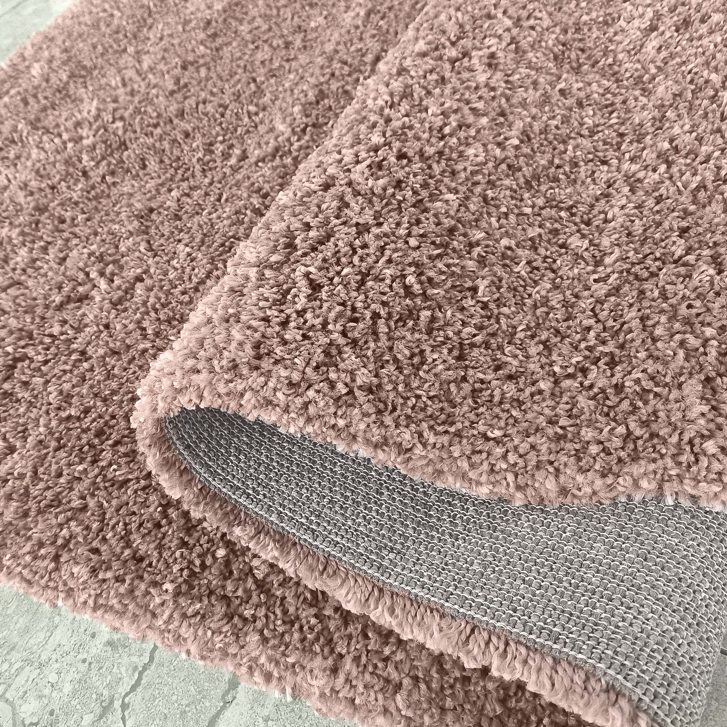 Tapis épais couleur beige rosé avec une texture moelleuse de longs poils bouclés, dont le revers gris est visible