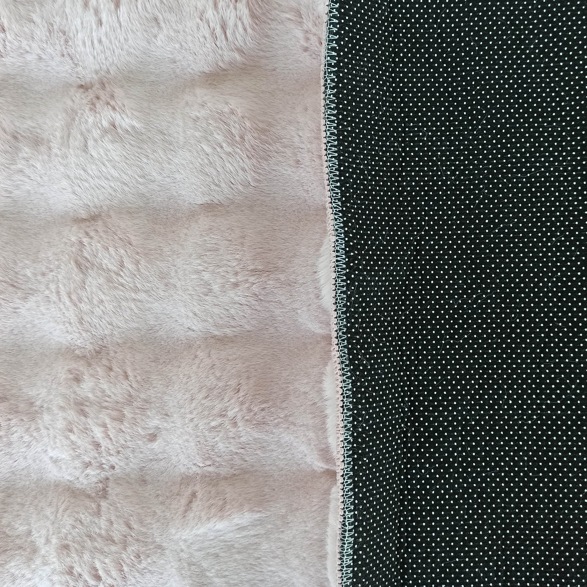 Tapis moelleux rose pâle avec une couture visible séparant un revers noir à petits pois blancs antidérapants