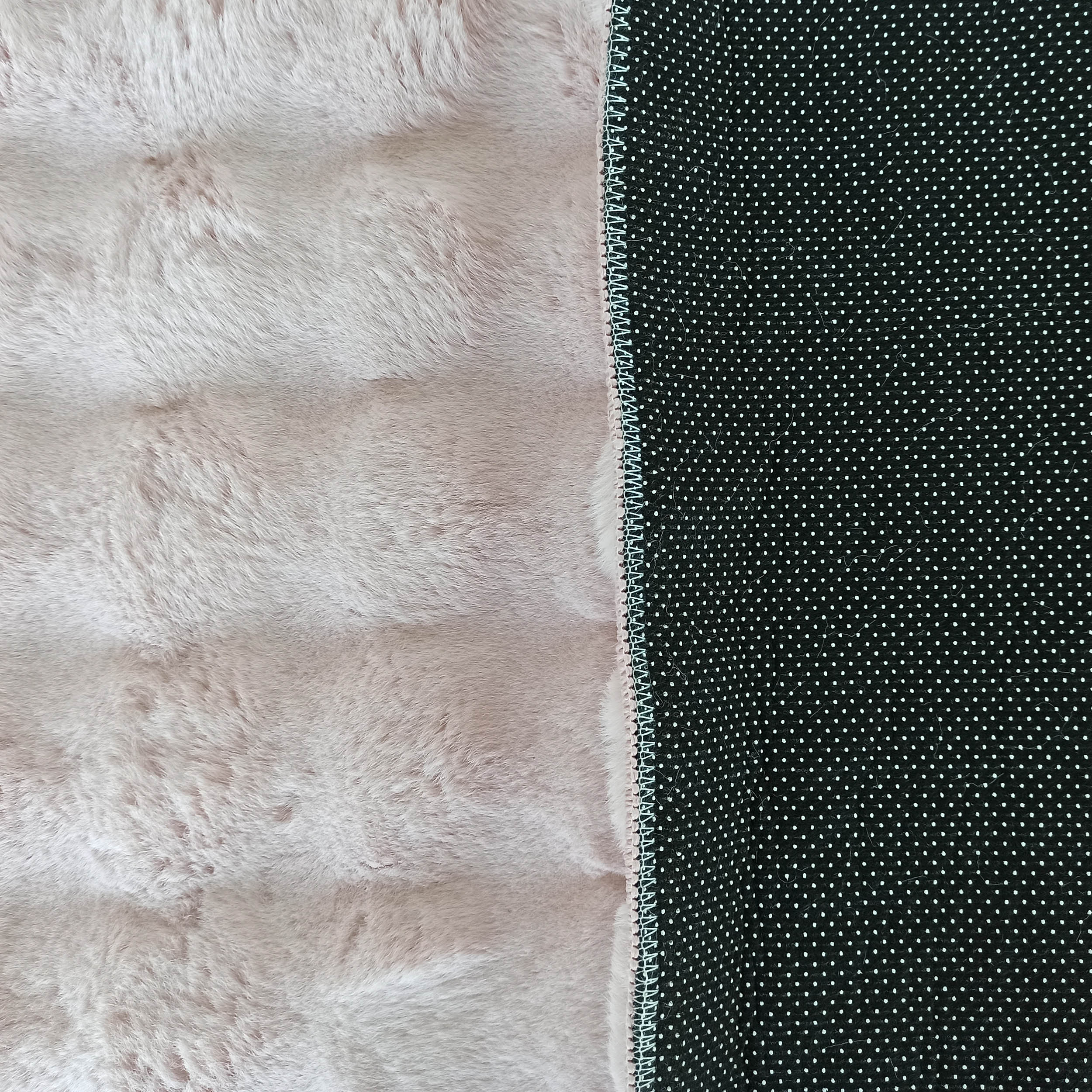 Tapis moelleux rose pâle avec une couture visible séparant un revers noir à petits pois blancs antidérapants