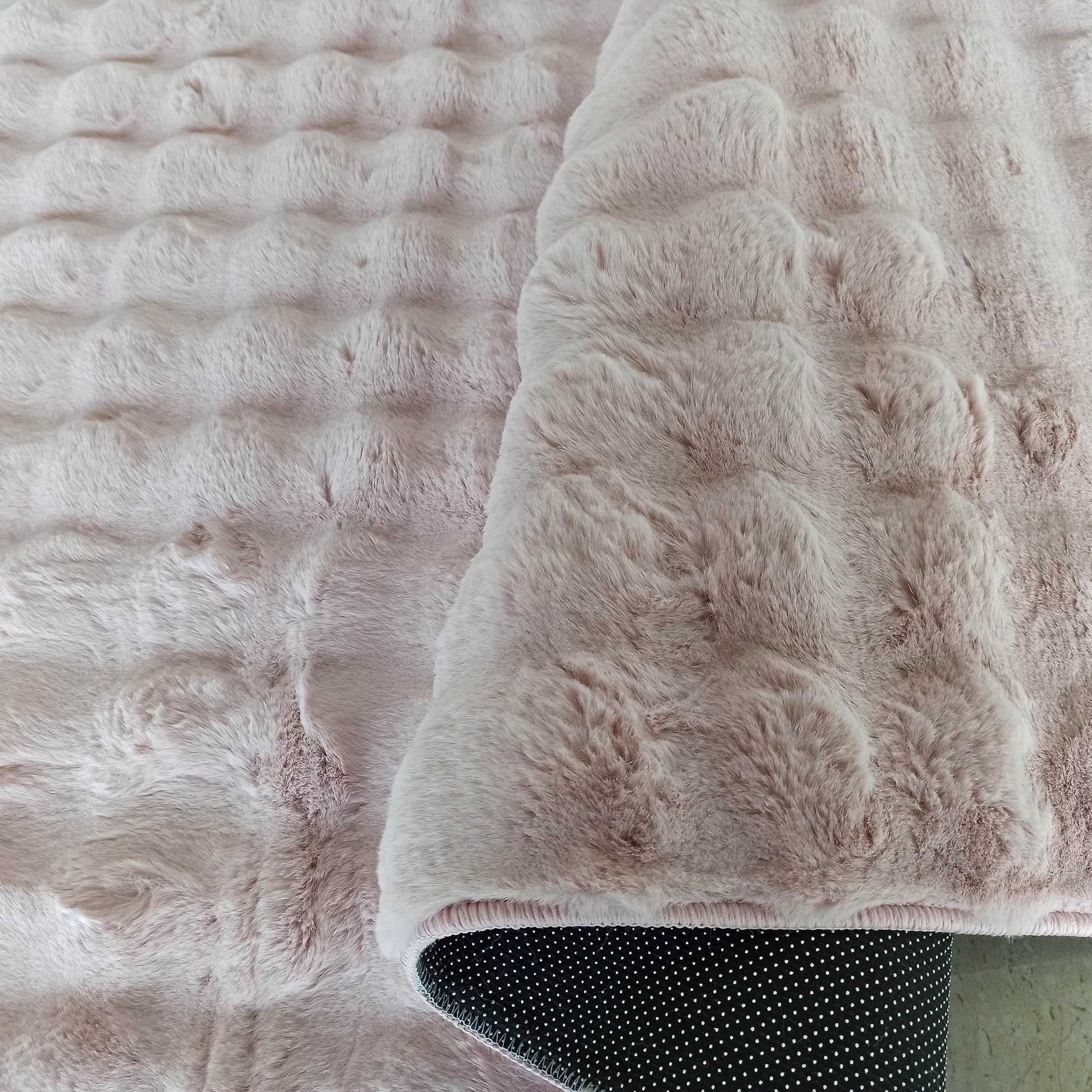 Tapis rose pâle et moelleux avec une surface en relief ondulée, le dessous noir à pois blancs est visible
