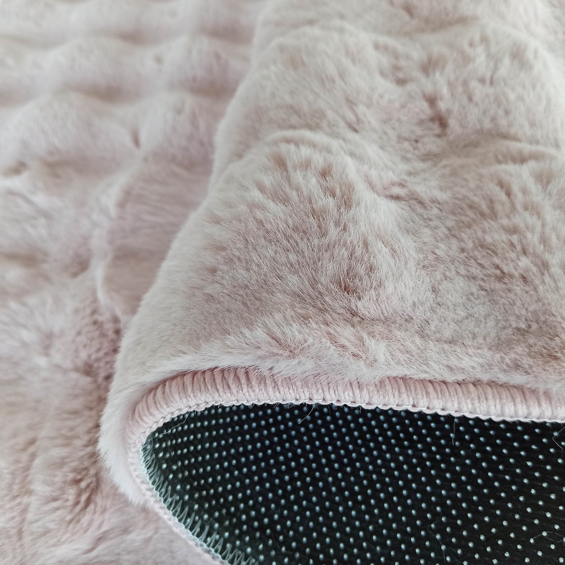 Tapis rose pâle à poils longs et texture douce. Le dessous antidérapant est noir à pois clairs, avec bordure rose