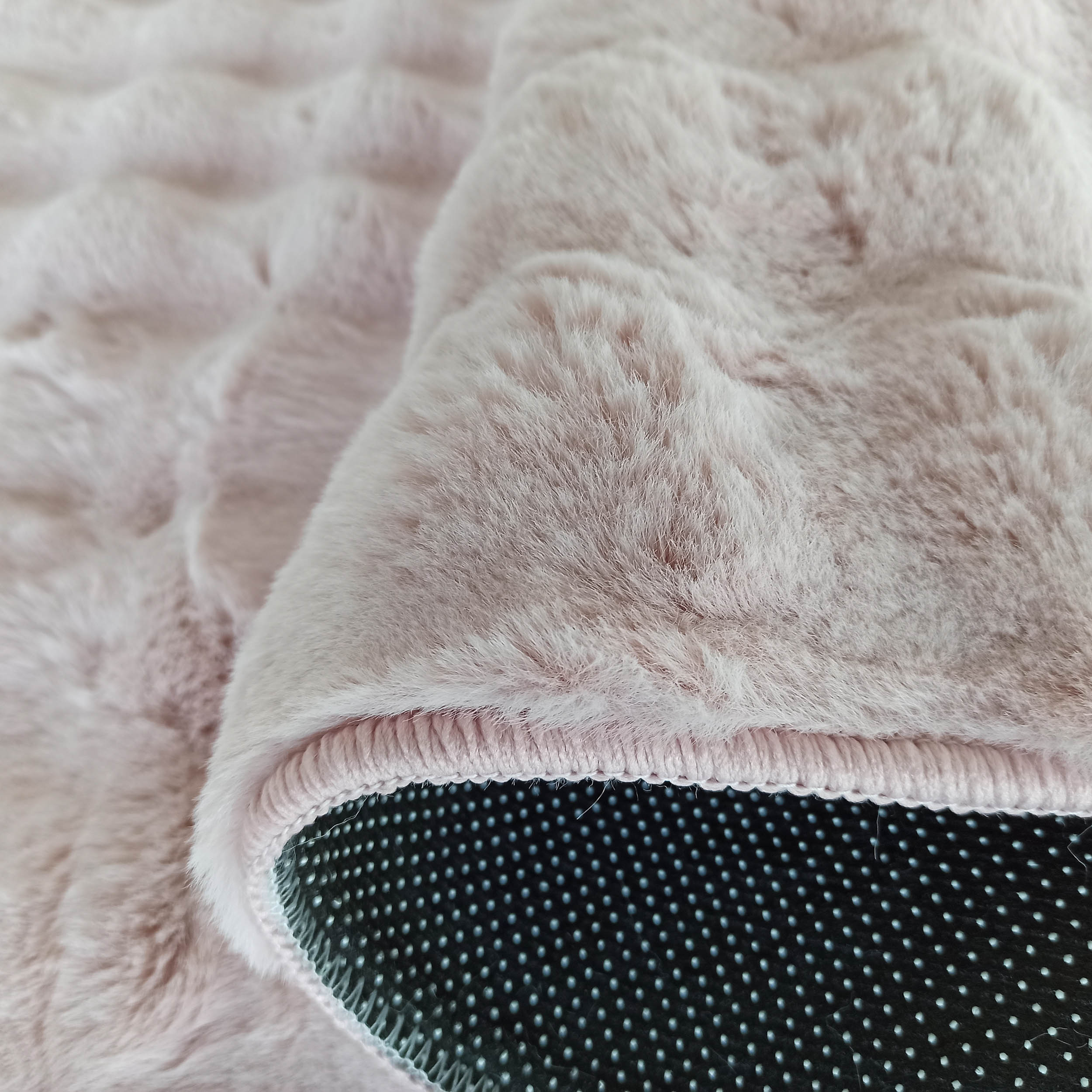 Tapis rose pâle à poils longs et texture douce. Le dessous antidérapant est noir à pois clairs, avec bordure rose