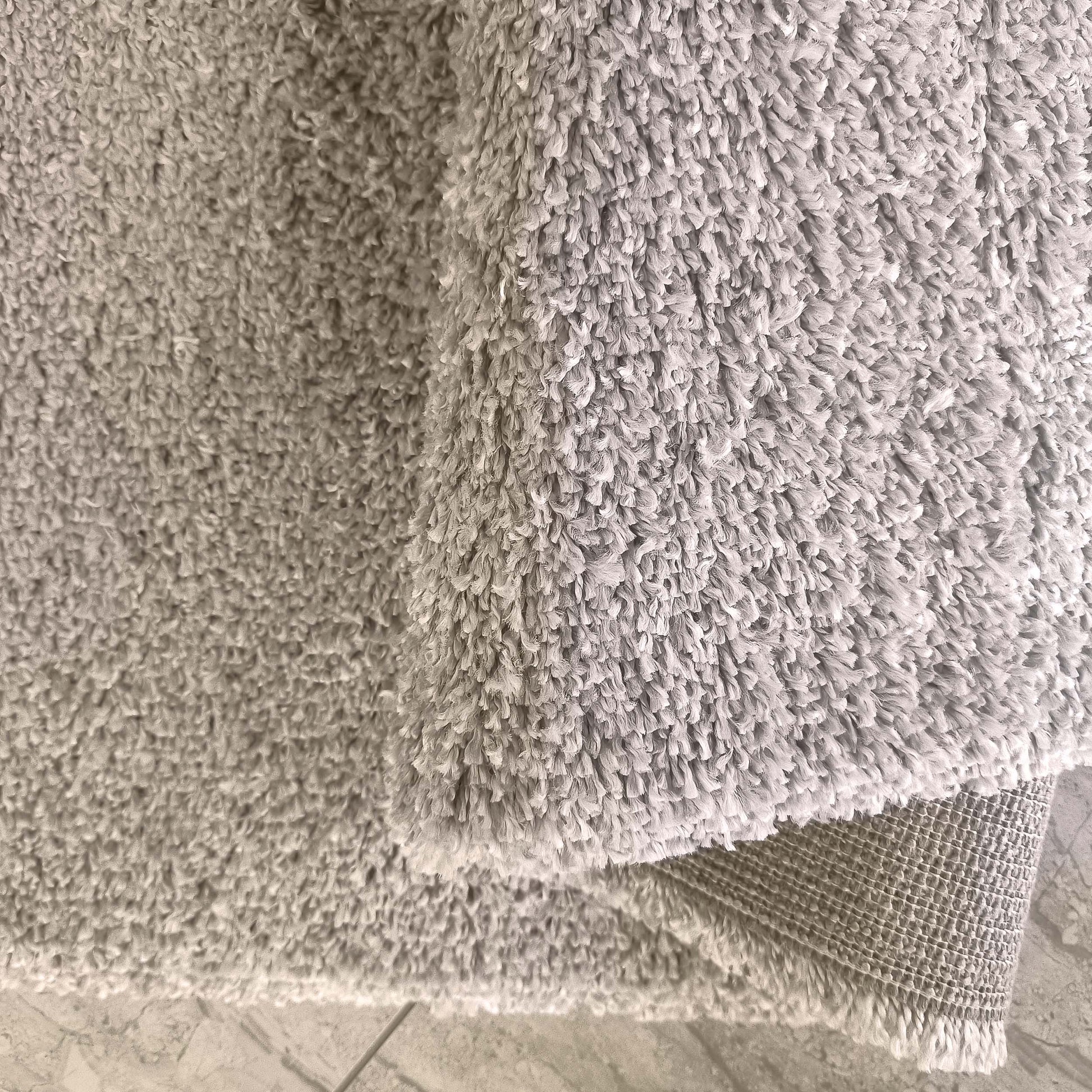 Tapis gris clair à la texture moelleuse et douce, partiellement roulé pour montrer son envers texturé