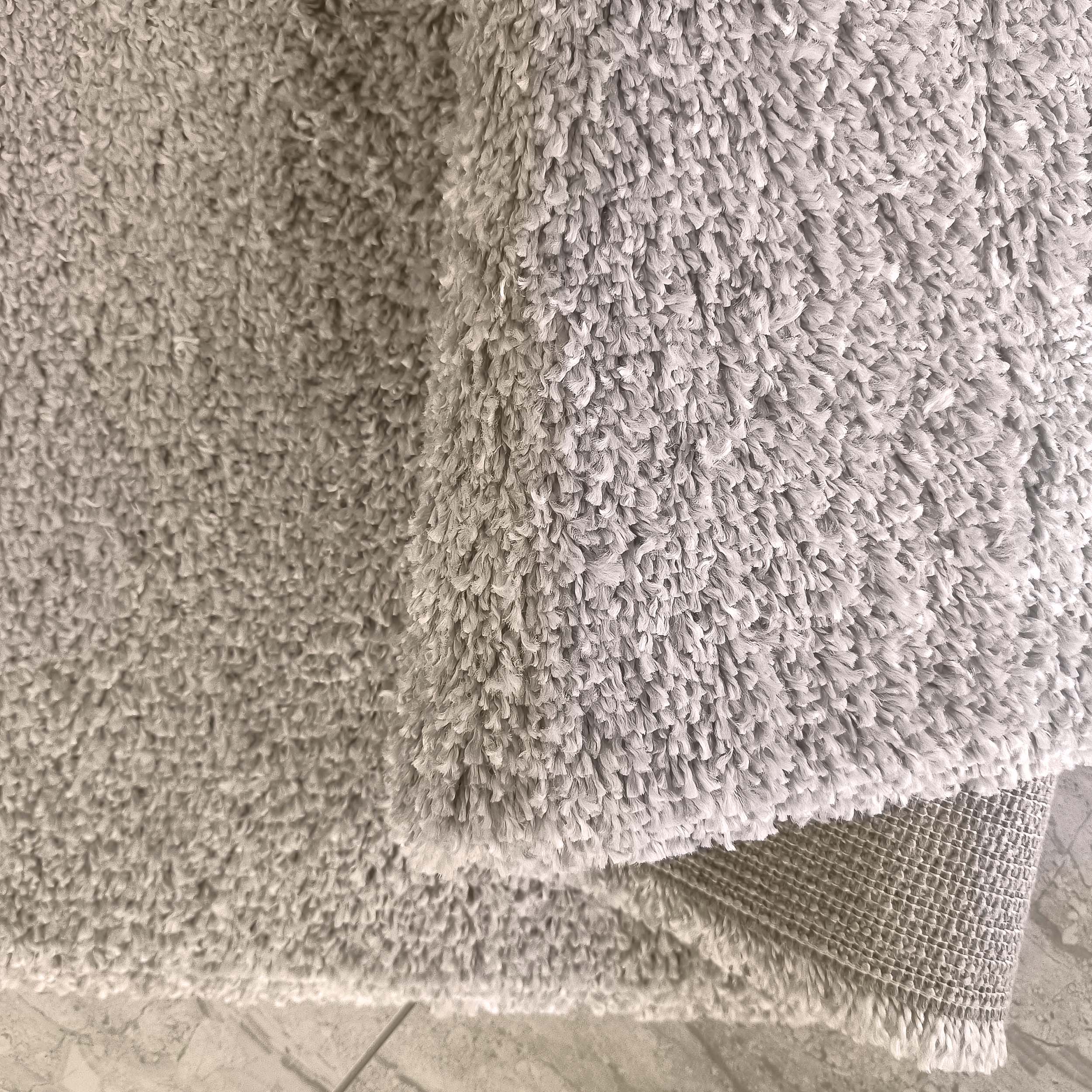 Tapis gris clair à la texture moelleuse et douce, partiellement roulé pour montrer son envers texturé