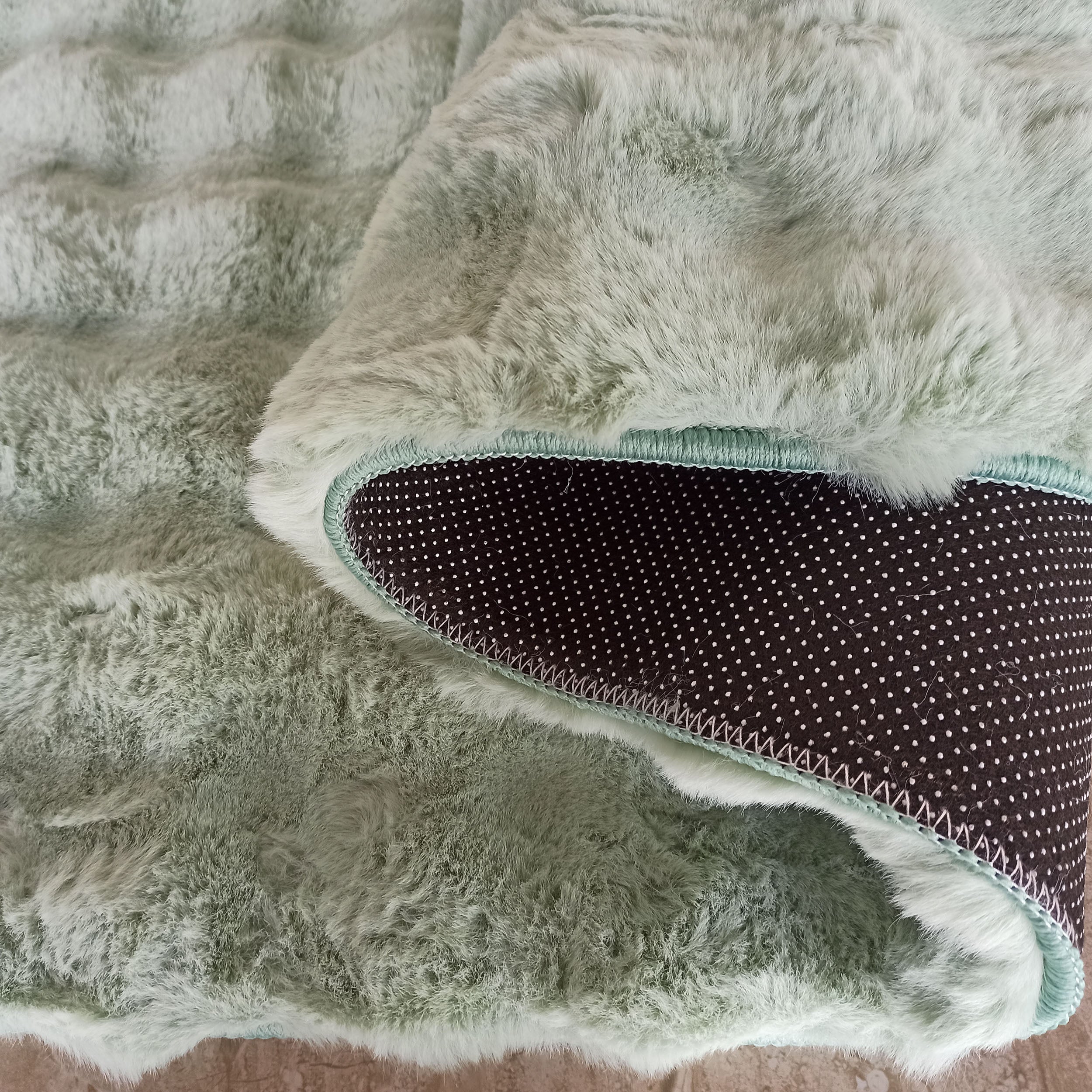 Tapis vert menthe moelleux et pelucheux, avec un coin replié révélant le dessous noir à petits pois blancs antidérapant