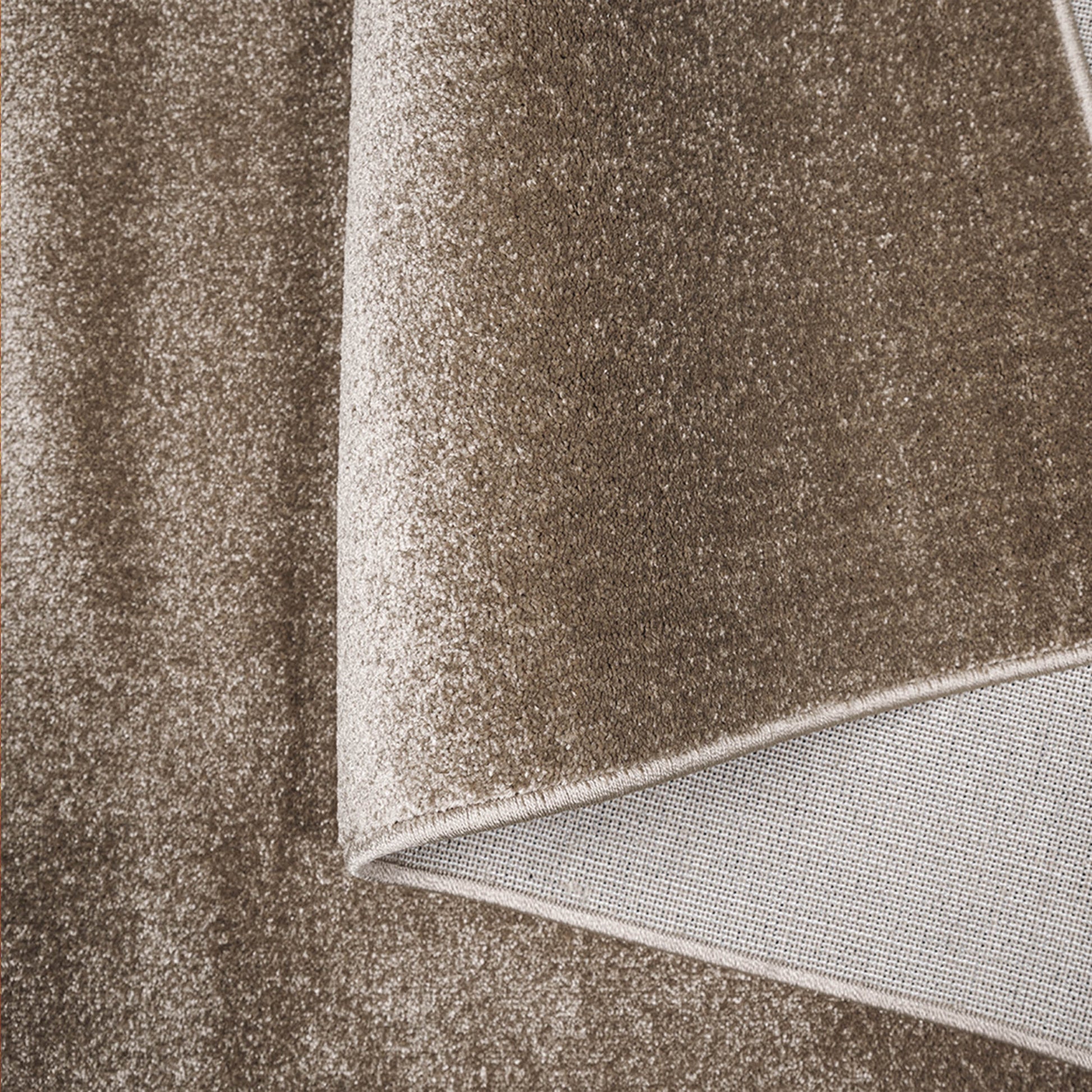 Tapis doux marron beige foncé avec un motif moucheté, replié pour montrer le dessous tissé clair et le bord cousu