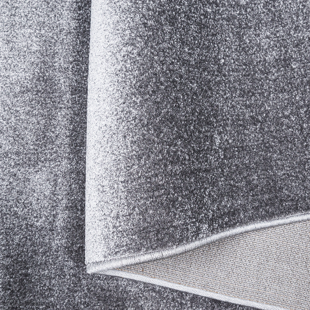 Tapis gris moucheté à la texture douce et légèrement poilue, avec un coin relevé dévoilant l'envers tissé