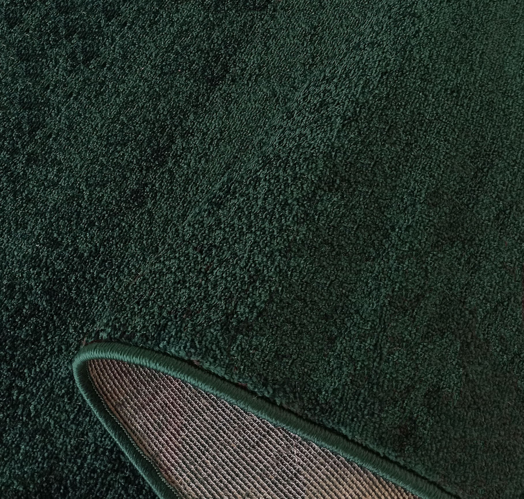 Tapis vert foncé à poils ras, avec un bord surpiqué du même ton et son envers tissé beige apparent