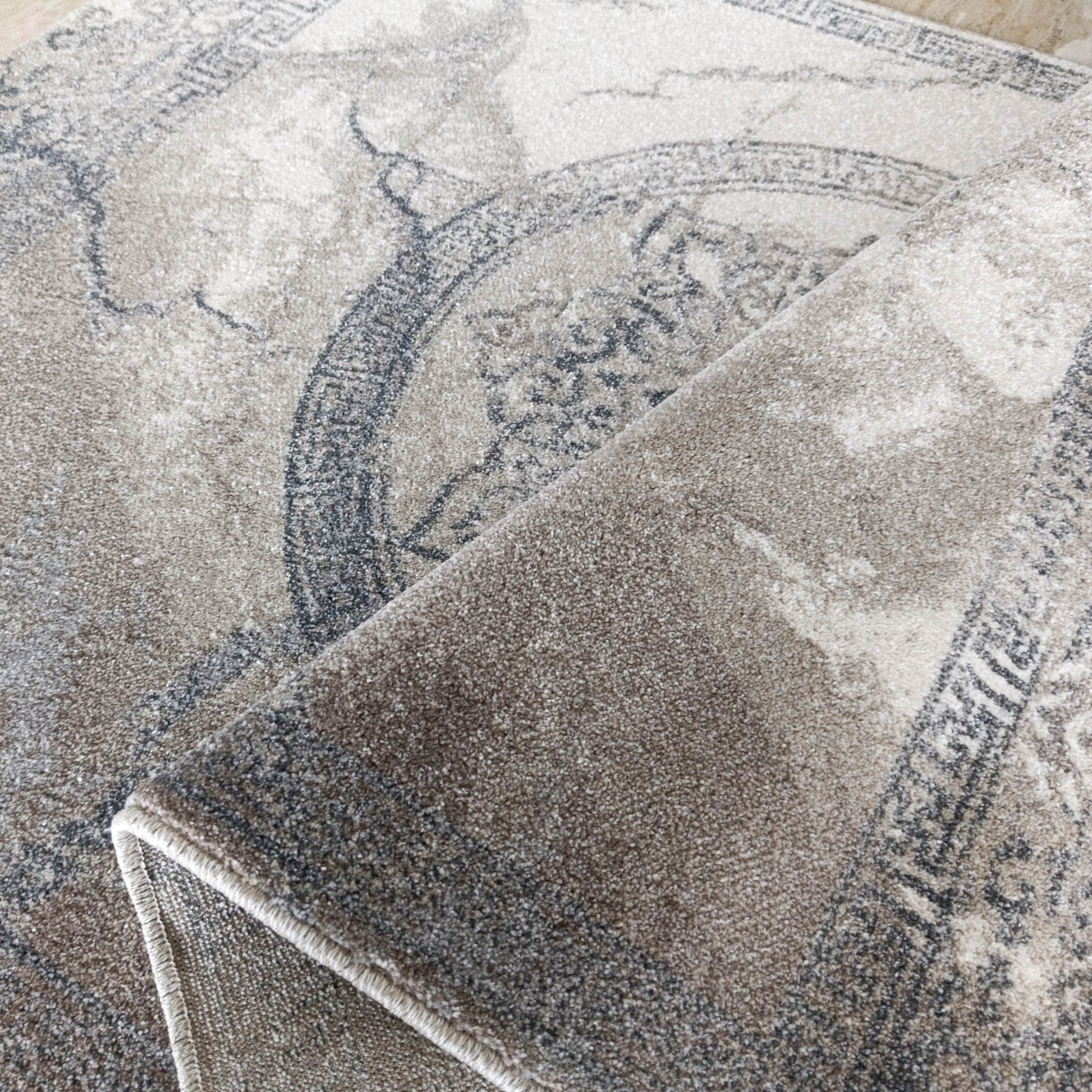 Tapis texturé beige et gris à motif circulaire ornemental et lignes vieillies, partiellement enroulé