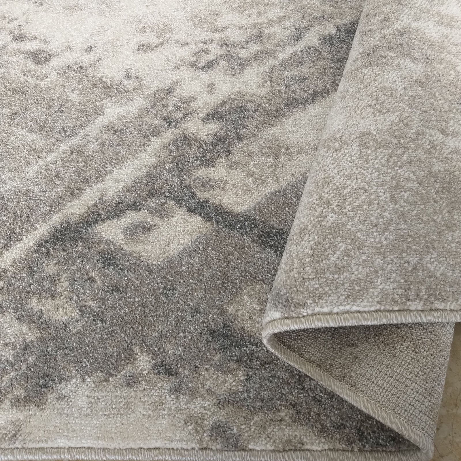 Tapis aux motifs délavés beiges et gris, avec le bord du tapis roulé exposant sa texture douce