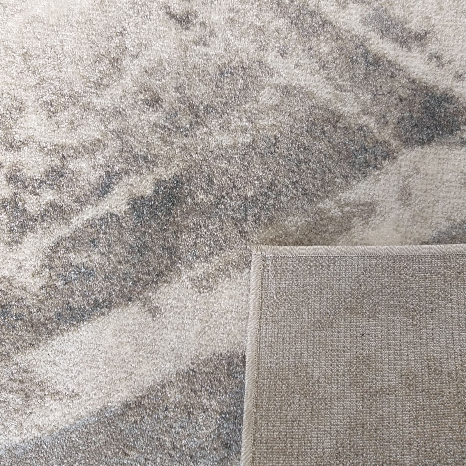 Tapis texturé doux aux motifs marbrés dans des tons de gris. Un coin relevé dévoile son envers tissé beige
