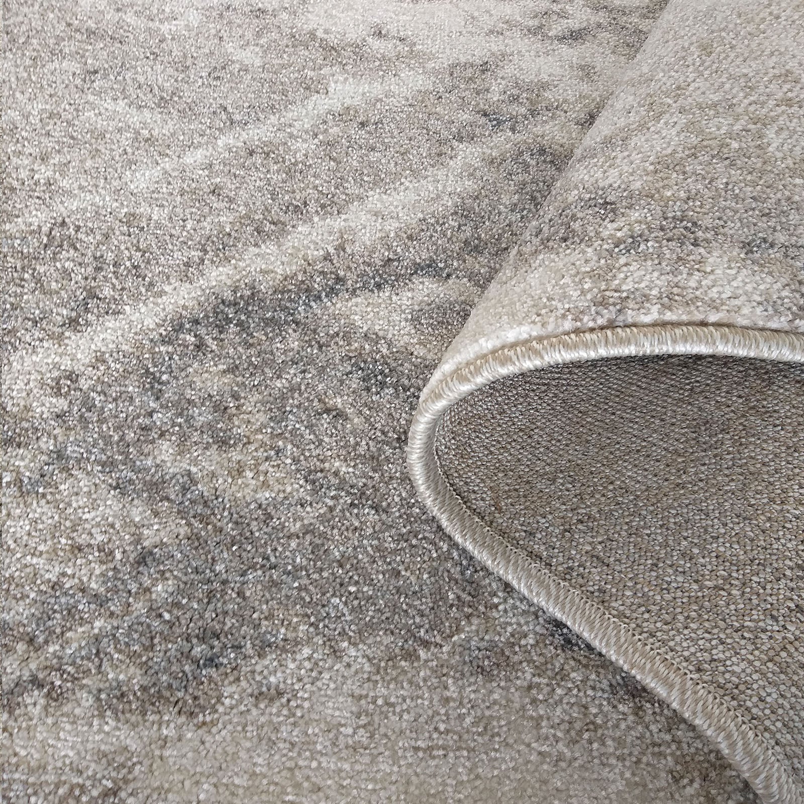 Tapis aux nuances de beige et gris, à motif abstrait moucheté, avec un bord roulé visible
