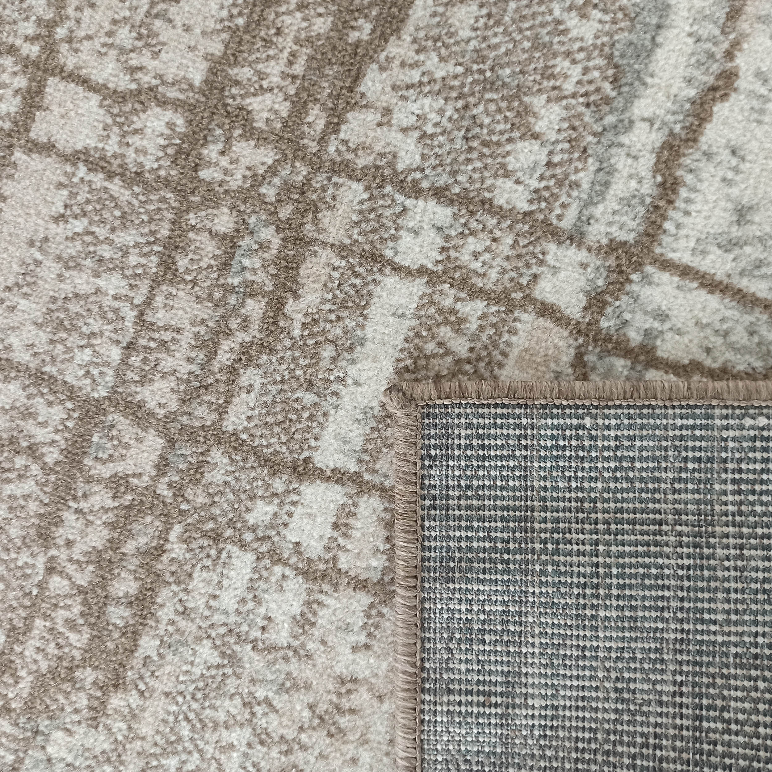 Tapis beige à motifs abstraits marron et texture douce avec un coin relevé qui dévoile son revers tissé quadrillé gris et blanc