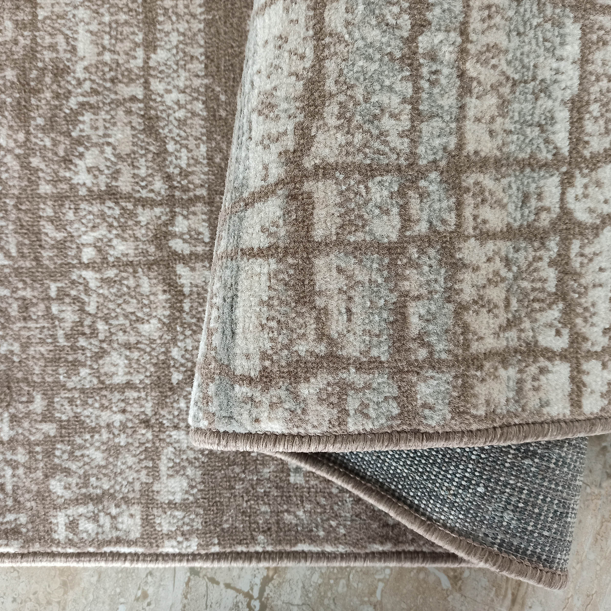 Tapis à l'aspect poilu aux tons marron, beige et gris, avec motifs abstraits, et une bande grise plus foncée en dessous