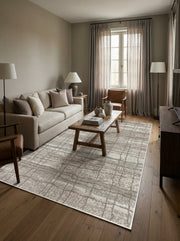Tapis rectangulaire beige clair avec un motif géométrique abstrait marron et texturé, posé sur un parquet dans un salon
