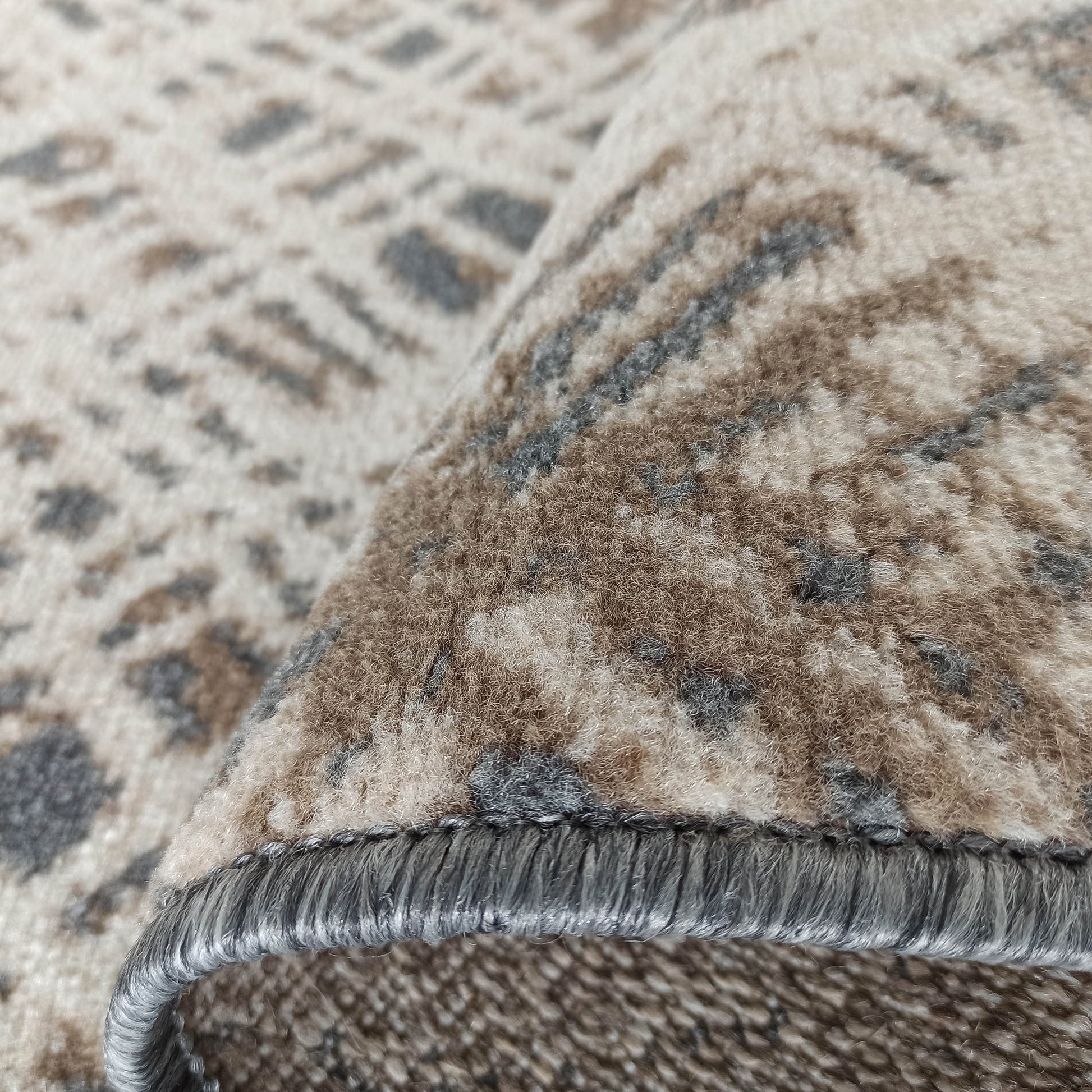 Gros plan sur un tapis doux aux motifs abstraits beige, marron et gris, révélant sa texture et son bord surjeté