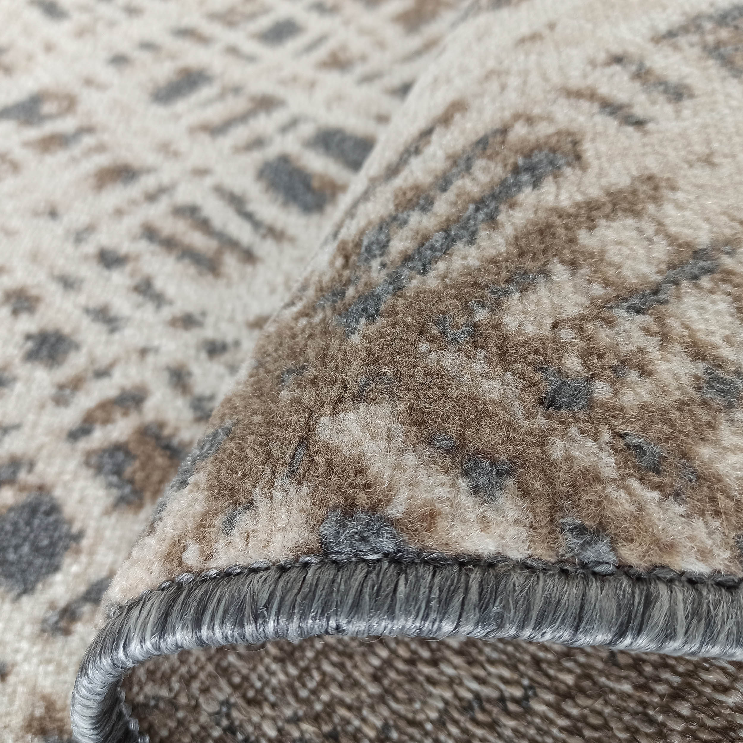 Gros plan sur un tapis doux aux motifs abstraits beige, marron et gris, révélant sa texture et son bord surjeté