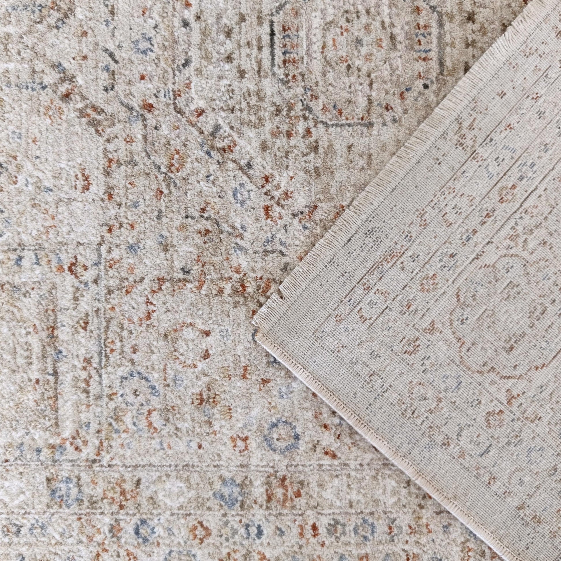 Tapis beige texturé avec motifs abstraits rouille et bleus, un coin est plié montrant l'envers tissé