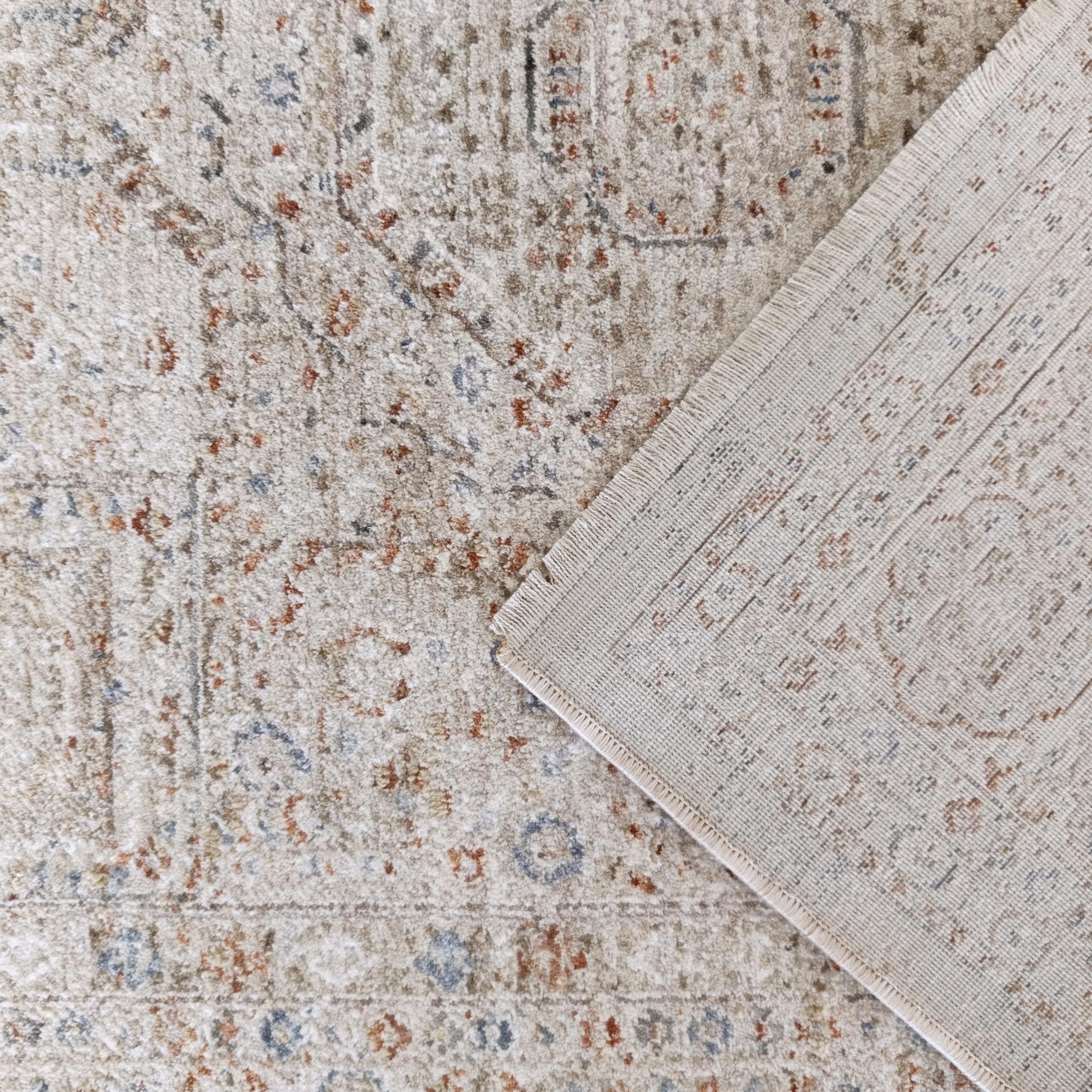 Tapis beige texturé avec motifs abstraits rouille et bleus, un coin est plié montrant l'envers tissé