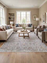 Tapis rectangulaire à motifs traditionnels vieillis en crème, bleu et terre cuite, avec franges. Il couvre le sol d'un salon