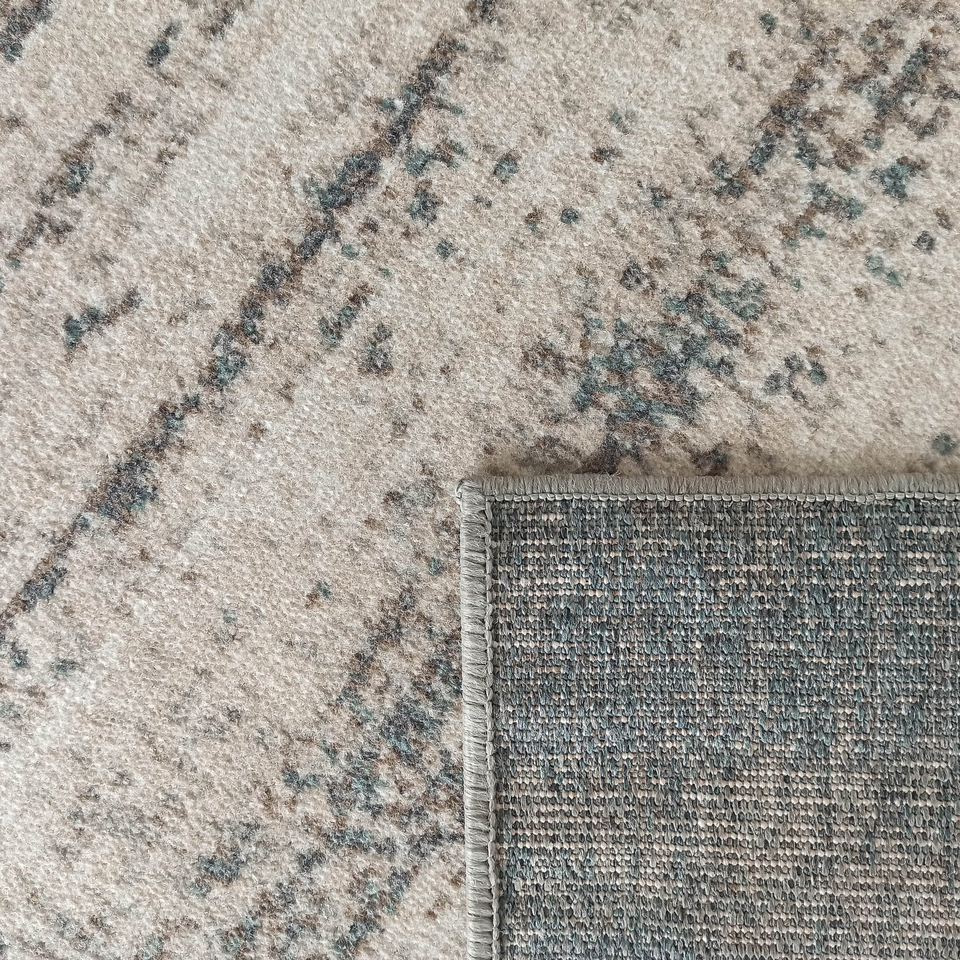 Tapis à poils courts beige clair avec des motifs abstraits marron et vert-de-gris, son envers tissé gris est visible