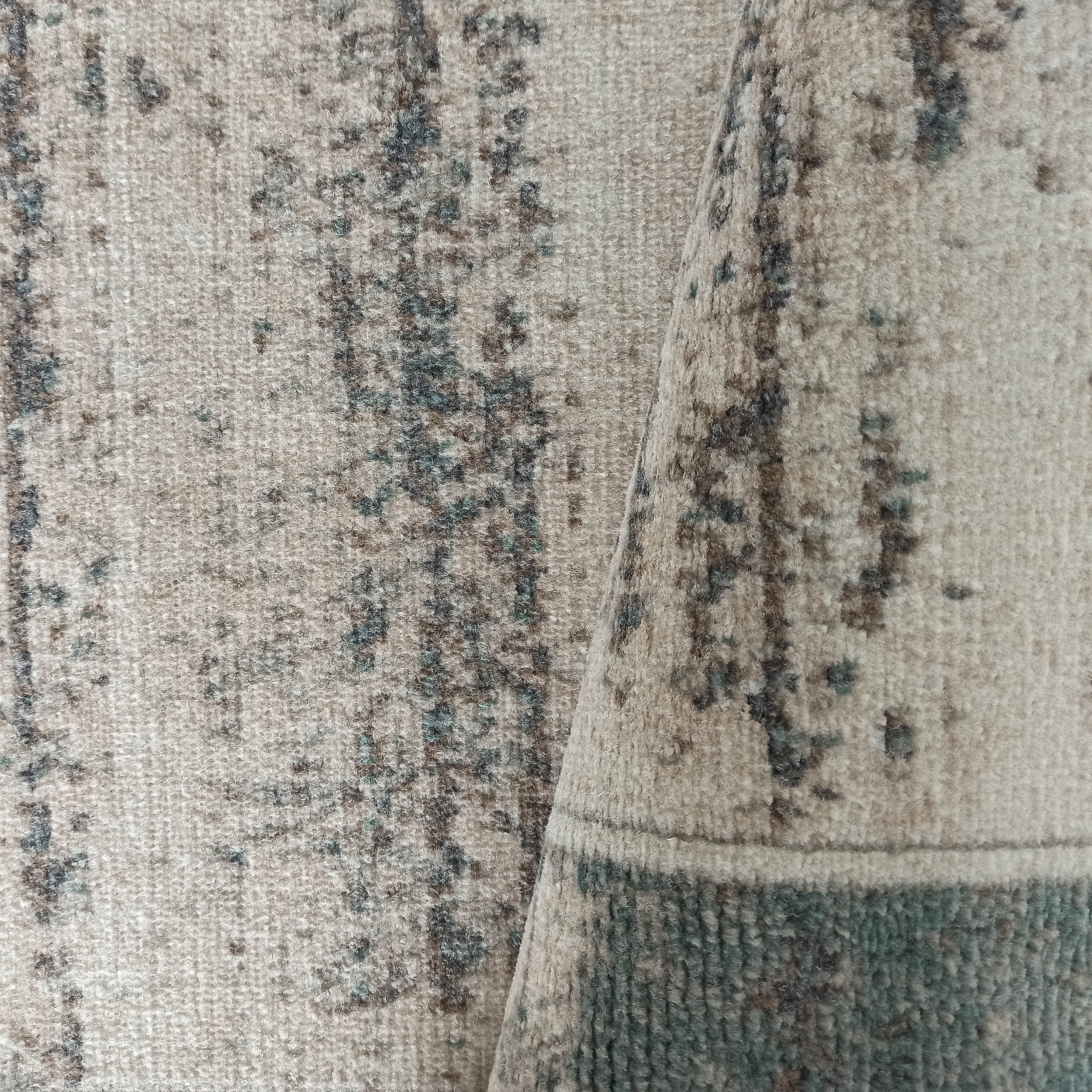 Tapis beige à motifs abstraits marron foncé et bleu canard, au toucher doux, dont une partie est repliée
