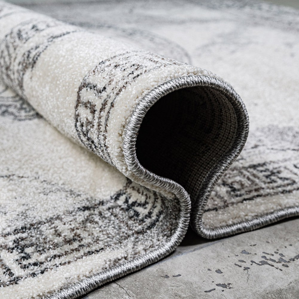 Tapis à poils courts crème et gris, à motifs délavés, partiellement roulé avec des bords surpiqués argentés