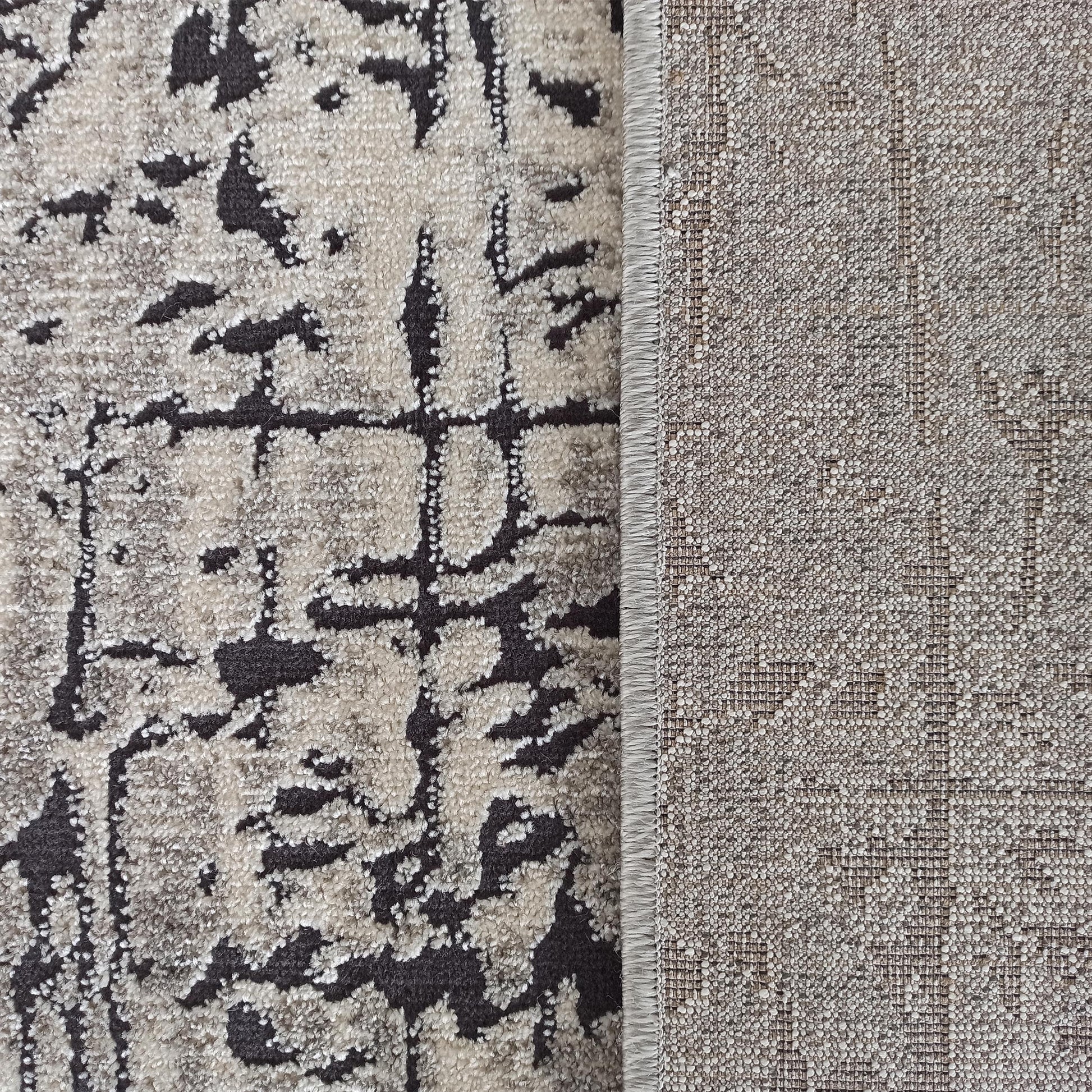Tapis texturé à poils doux beige clair et motifs abstraits gris foncé, avec son envers tissé visible