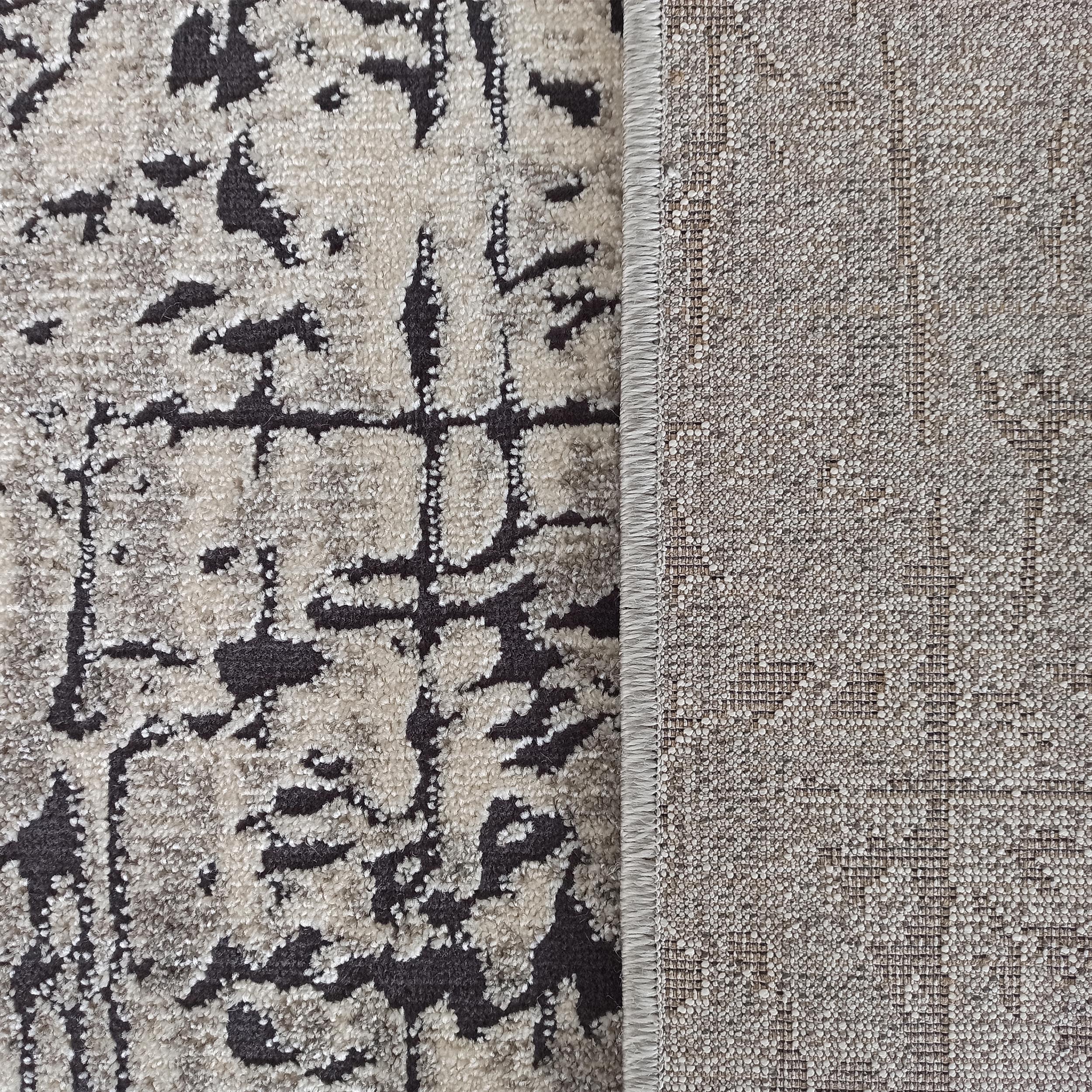 Tapis texturé à poils doux beige clair et motifs abstraits gris foncé, avec son envers tissé visible