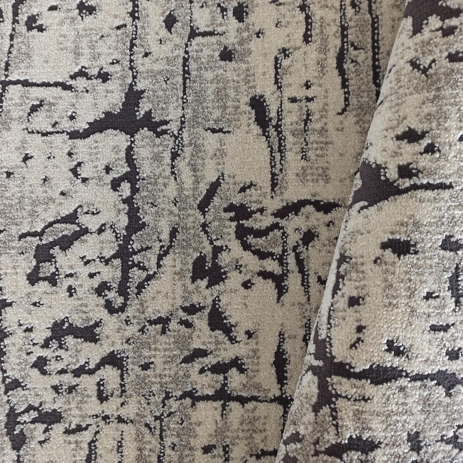 Tapis texturé doux aux motifs abstraits gris foncé sur fond beige clair, partiellement roulé