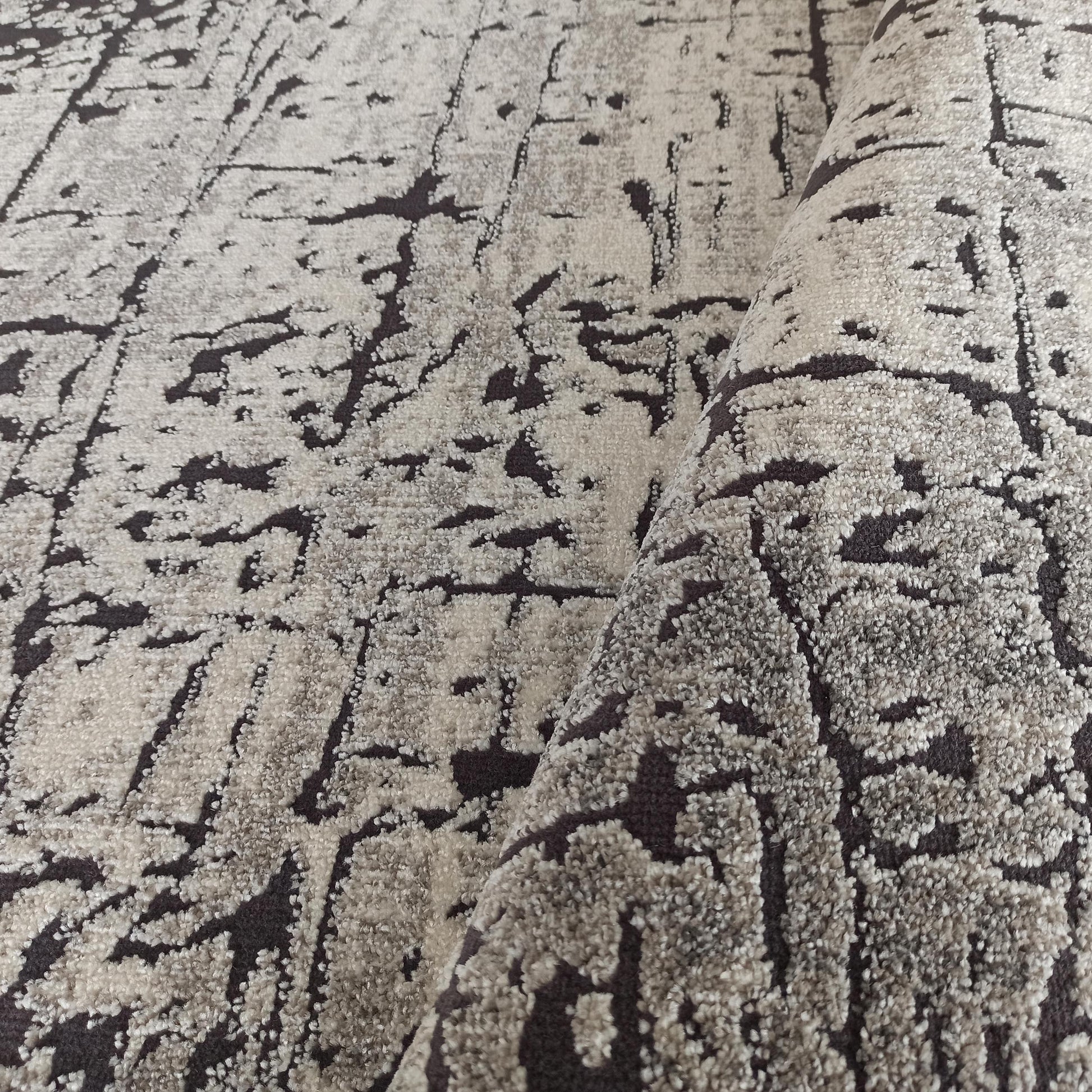 Tapis aux motifs abstraits beige clair et brun foncé, avec une texture dense et bouclée, partiellement roulé