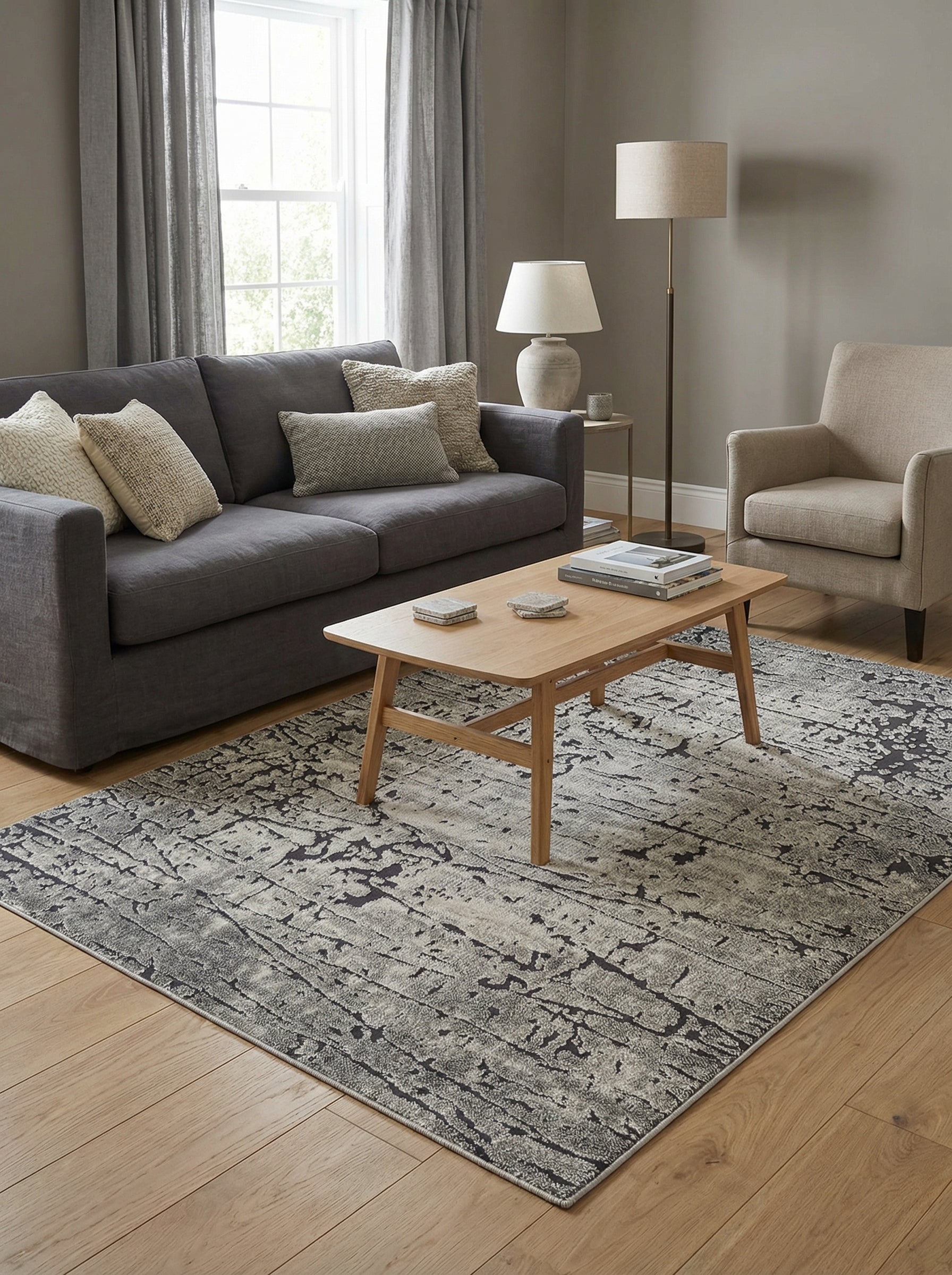 Tapis rectangulaire aux motifs abstraits gris et anthracite, évoquant une texture usée, posé sur un parquet clair dans un salon moderne