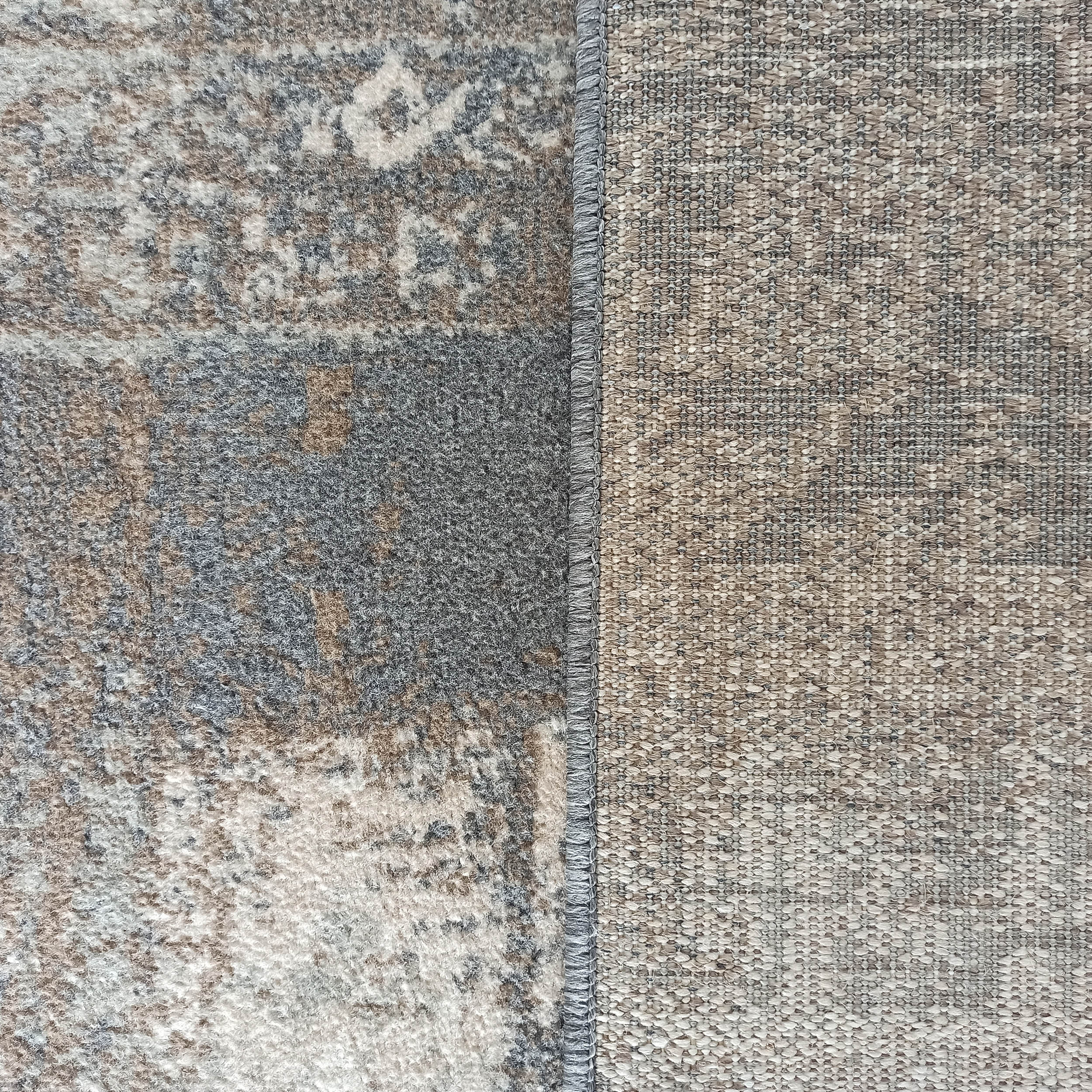 Vue rapprochée d'un tapis montrant la surface supérieure grise et beige à motifs, séparée par une couture grise de l'envers tissé