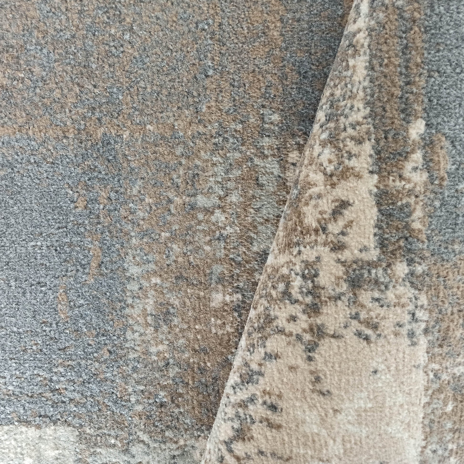 Tapis à la texture poilue et aux motifs abstraits mélangeant le gris, le beige et le blanc cassé, avec un grand pli