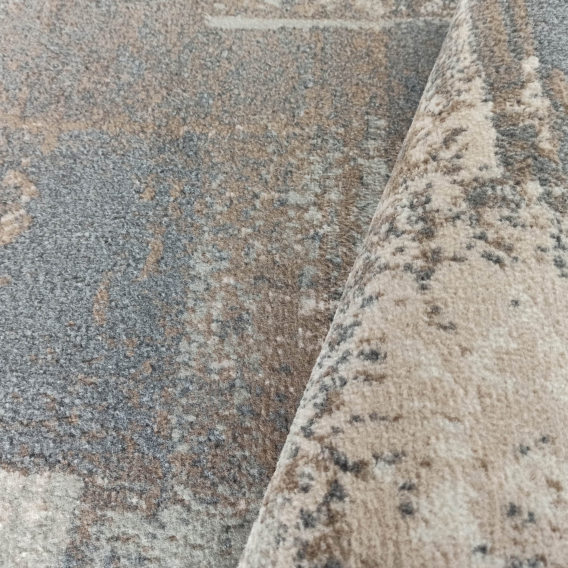 Tapis moderne à la texture douce et aux motifs abstraits marbrés, dans un camaïeu de gris, beige et brun, plié sur un côté