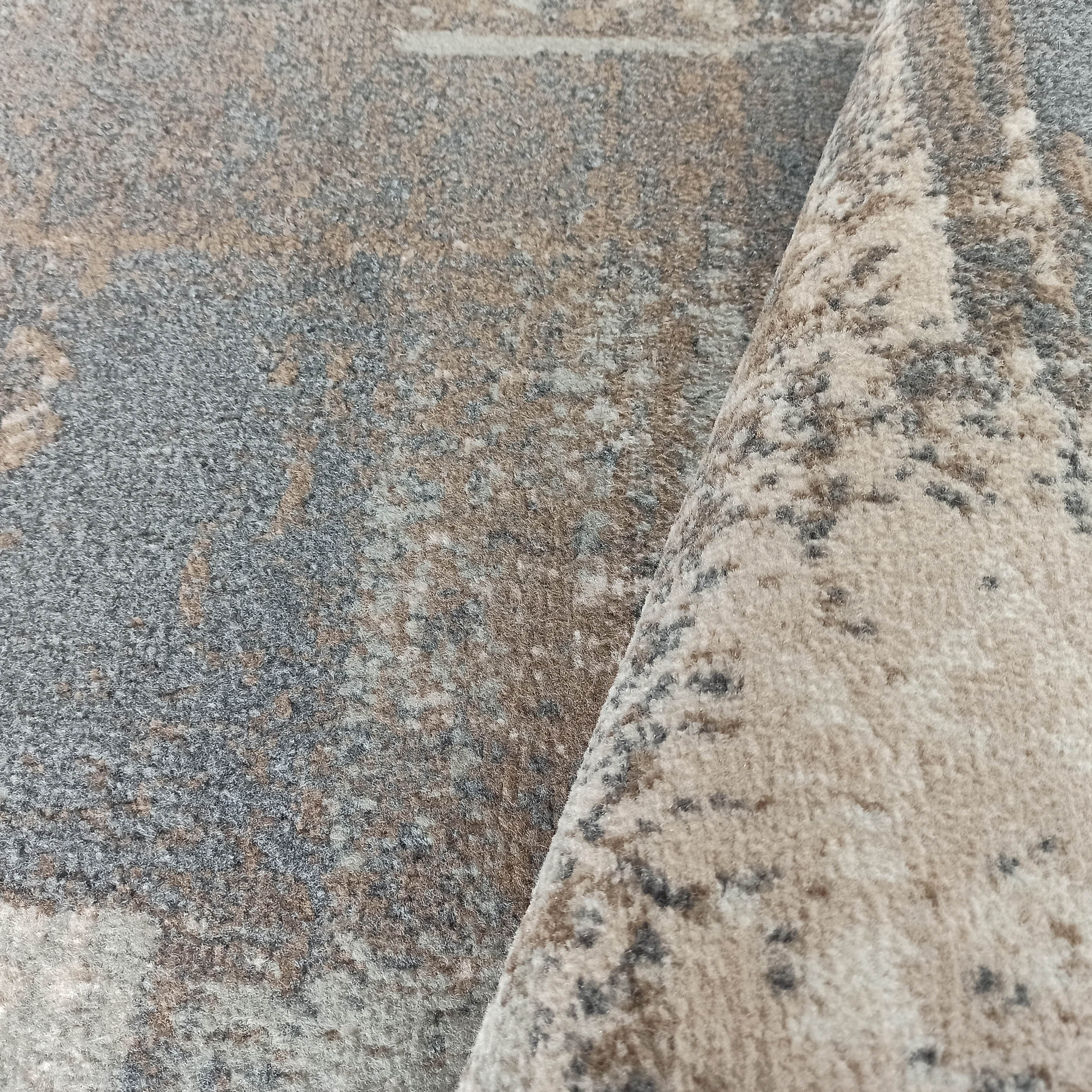 Tapis moderne à la texture douce et aux motifs abstraits marbrés, dans un camaïeu de gris, beige et brun, plié sur un côté
