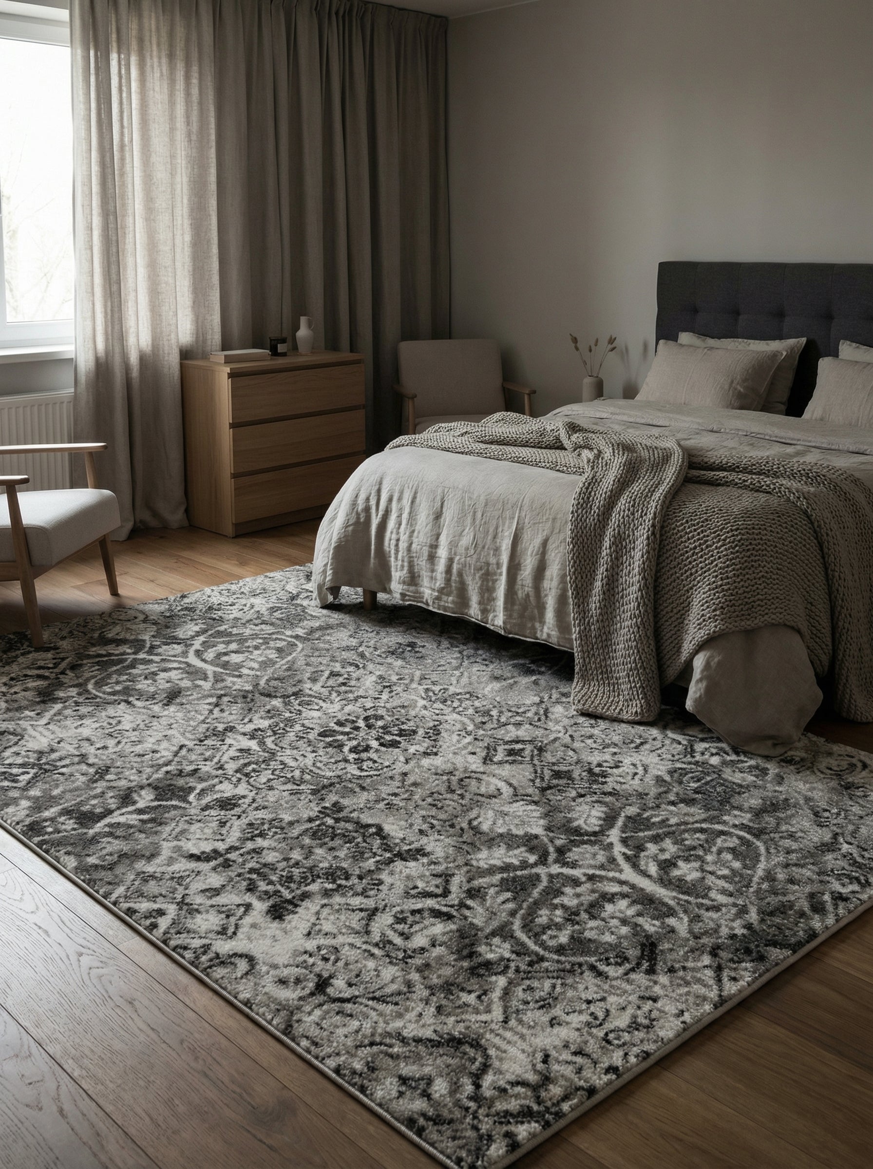 Grand tapis gris aux motifs ornementaux délavés en nuances claires et foncées, couvrant le sol d'une chambre