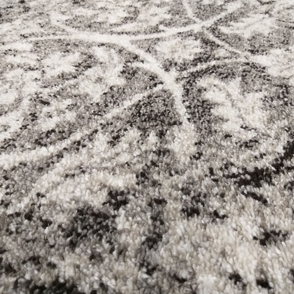 Tapis moelleux aux tons de gris, blanc et noir, présentant des motifs abstraits et une texture douce à l'aspect vieilli