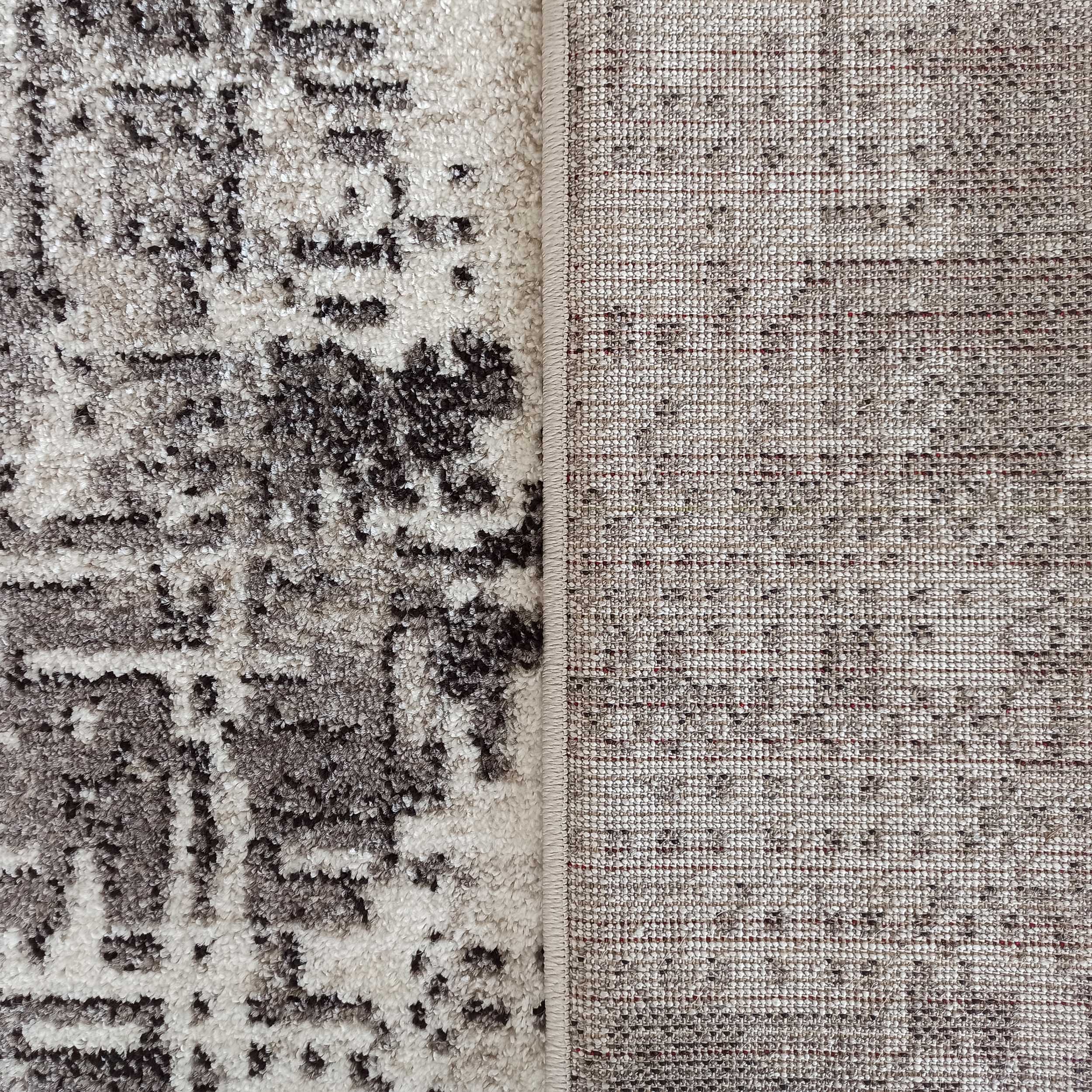 Tapis beige et gris à motifs abstraits sur le dessus, montrant aussi son envers tissé à texture fine