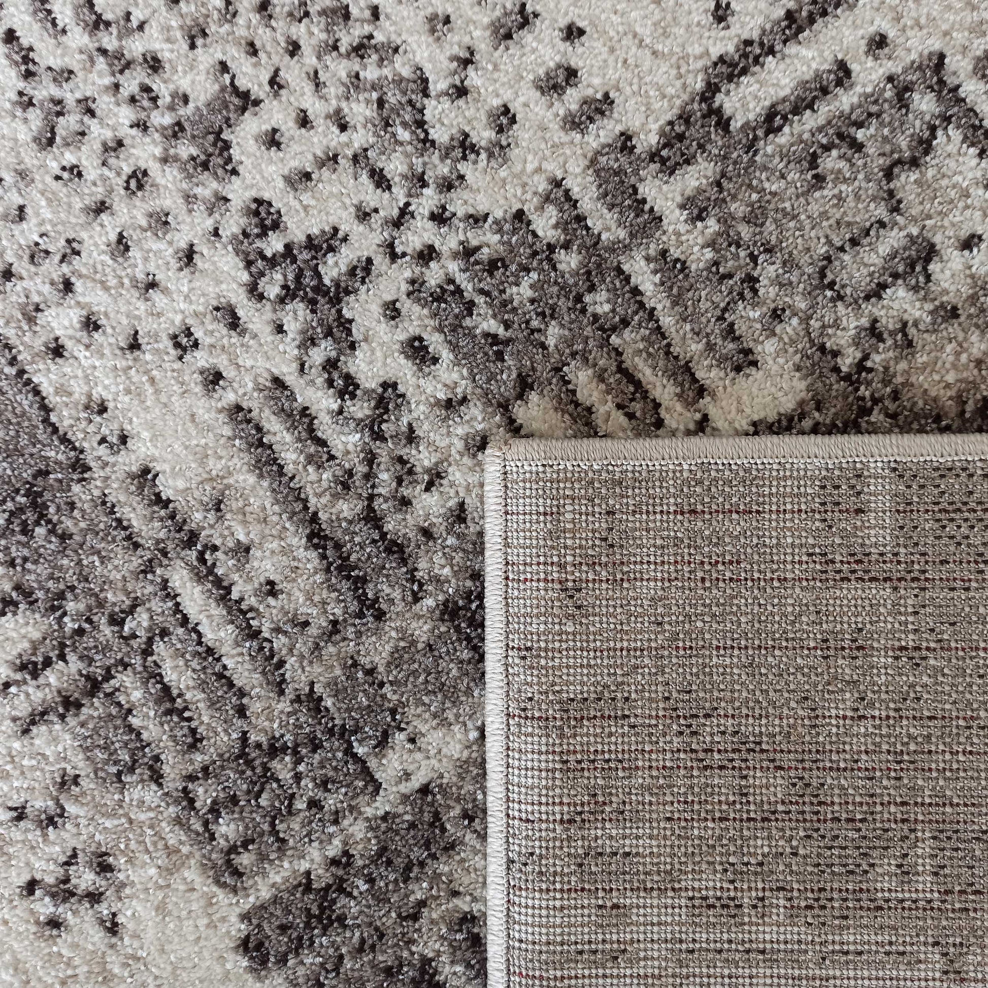 Tapis à motifs abstraits crème et gris, à l'aspect doux et texturé. Le coin relevé montre son dos tissé