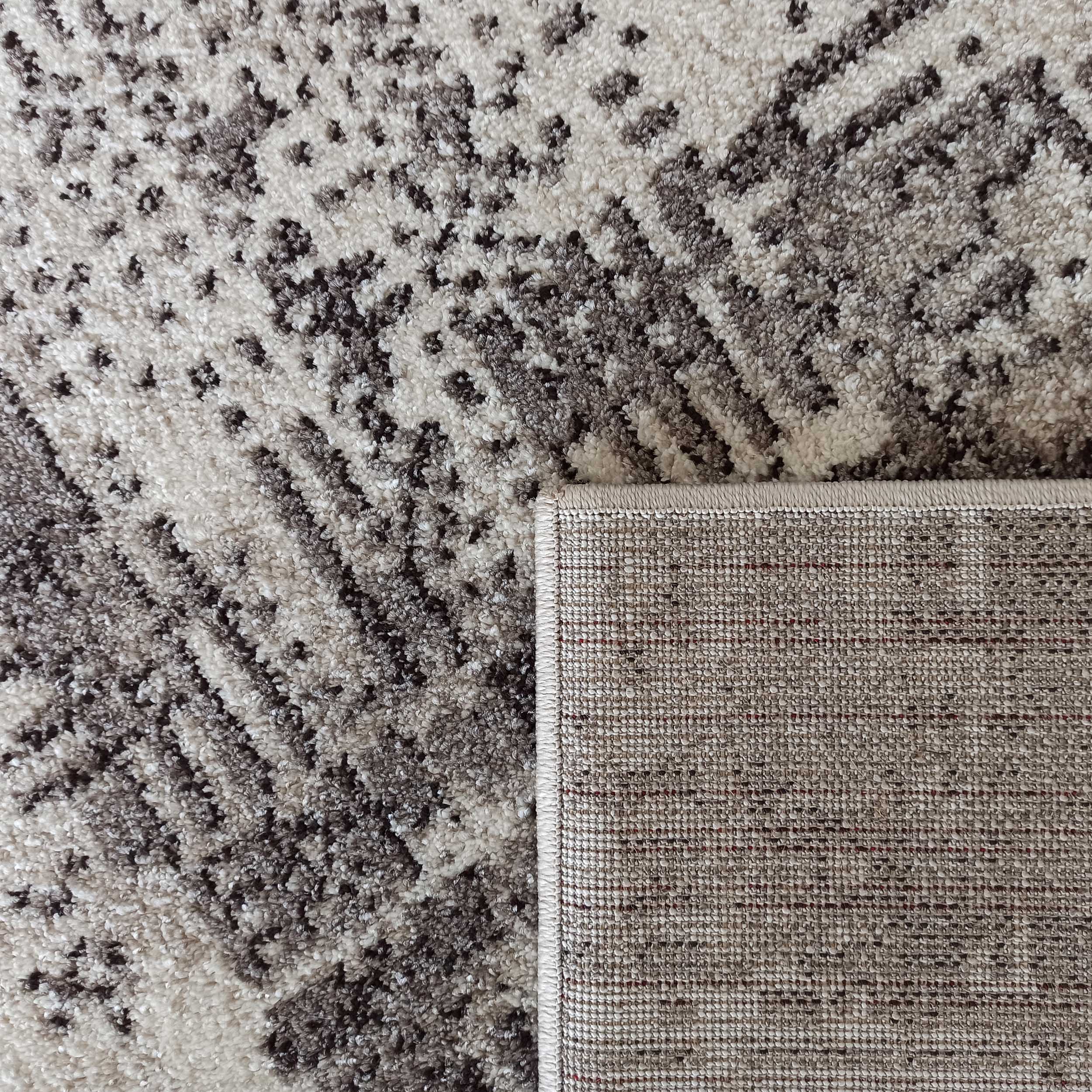 Tapis à motifs abstraits crème et gris, à l'aspect doux et texturé. Le coin relevé montre son dos tissé