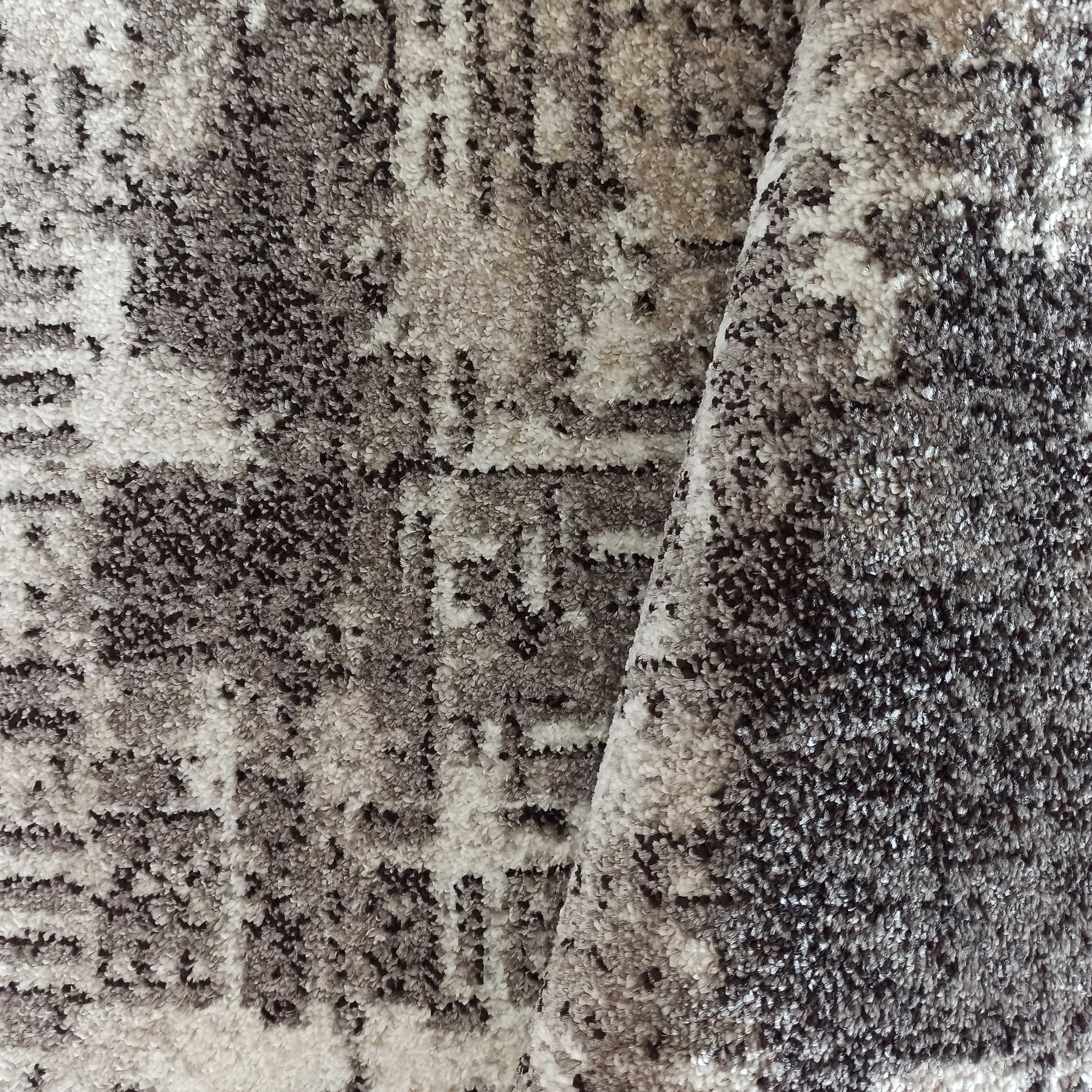 Tapis à poils longs et épais, avec un motif abstrait en nuances de gris, blanc et noir, une partie est pliée
