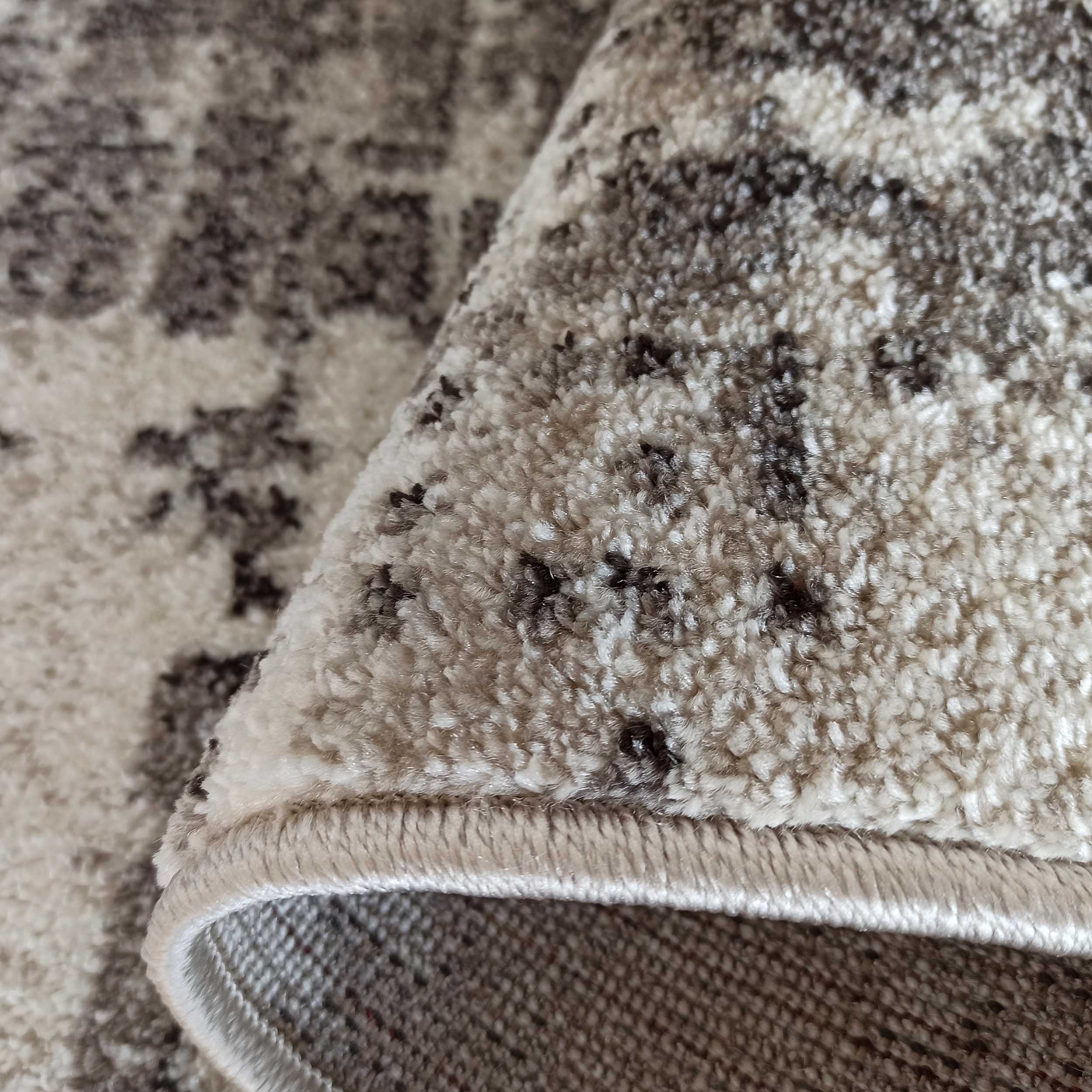 Gros plan sur un tapis enroulé aux poils longs et doux, avec un motif abstrait beige et gris foncé