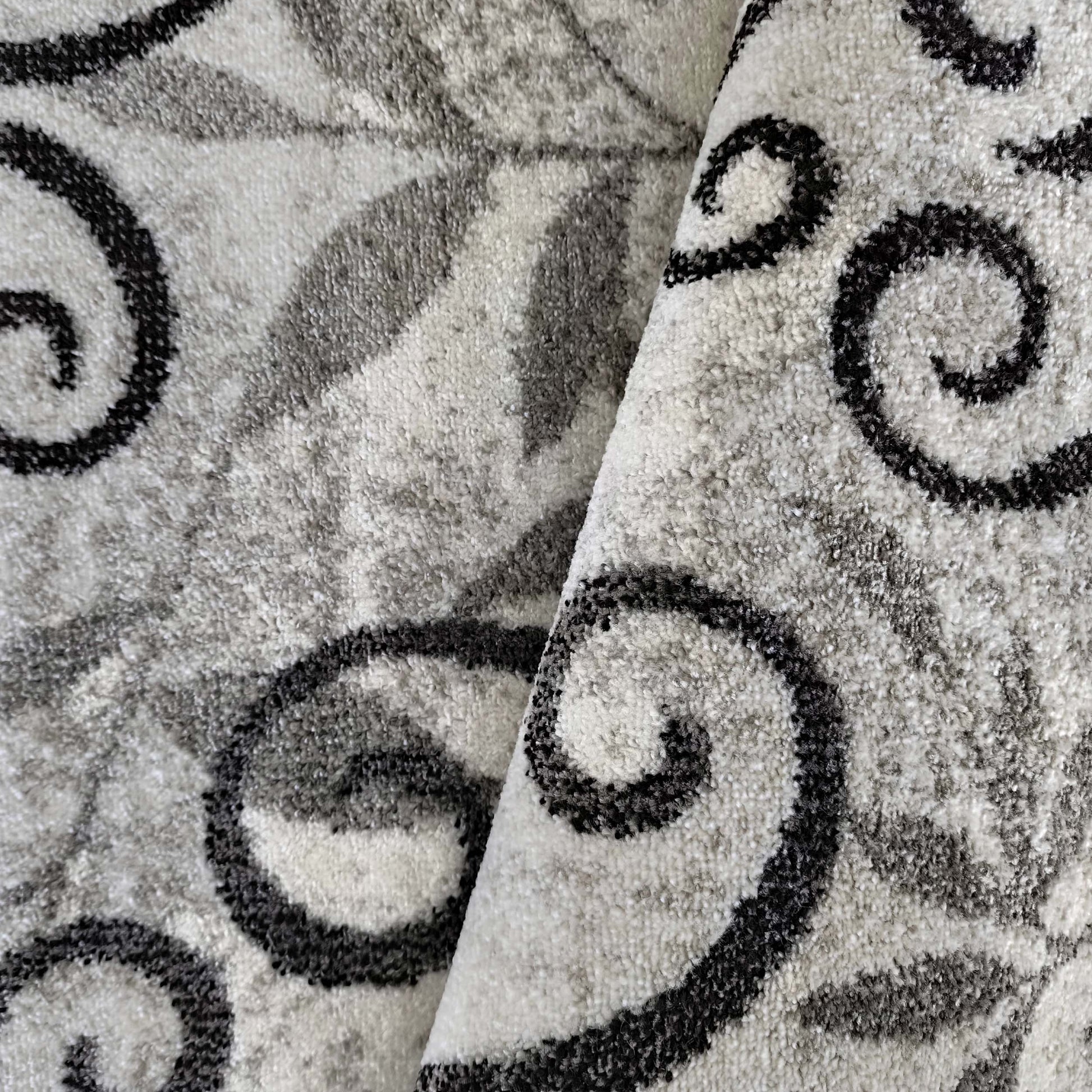 Gros plan sur un tapis texturé gris et blanc, orné de volutes noires et de motifs végétaux flous