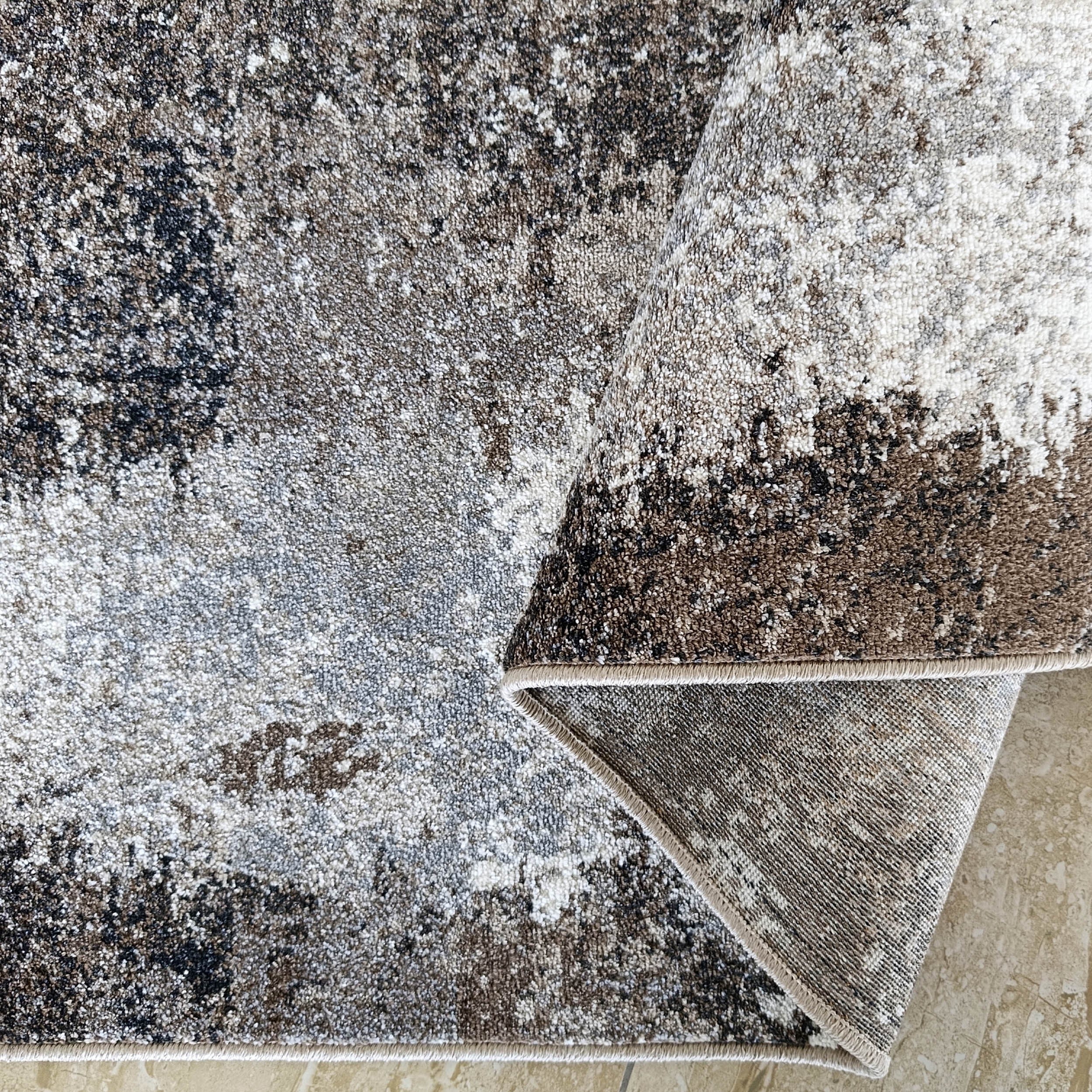 Un tapis à poil court abstrait marron, noir, blanc et gris est partiellement roulé sur carrelage beige