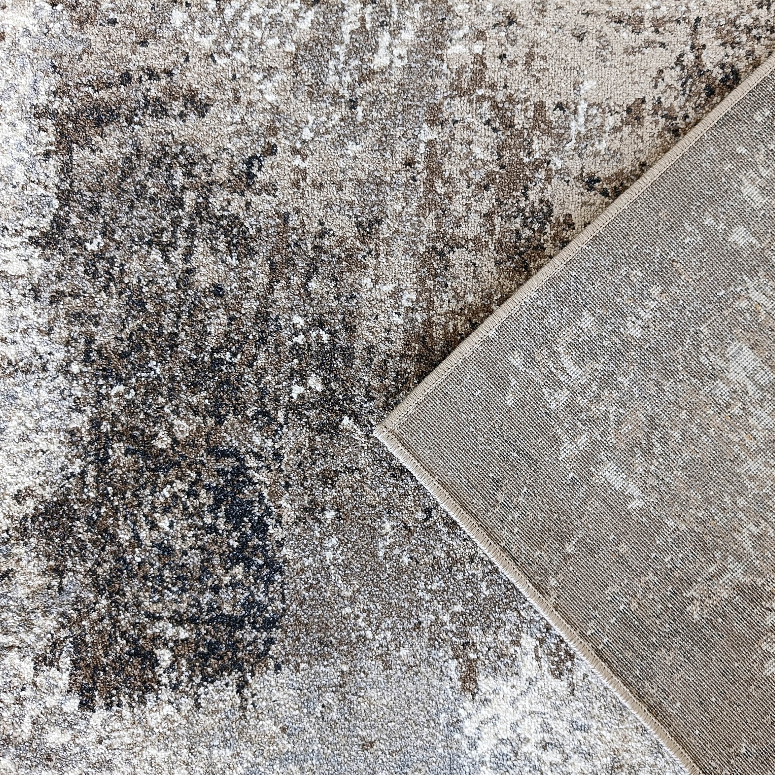 Tapis à motifs abstraits mouchetés blancs, beiges, marron et noirs, un coin replié montrant l'envers