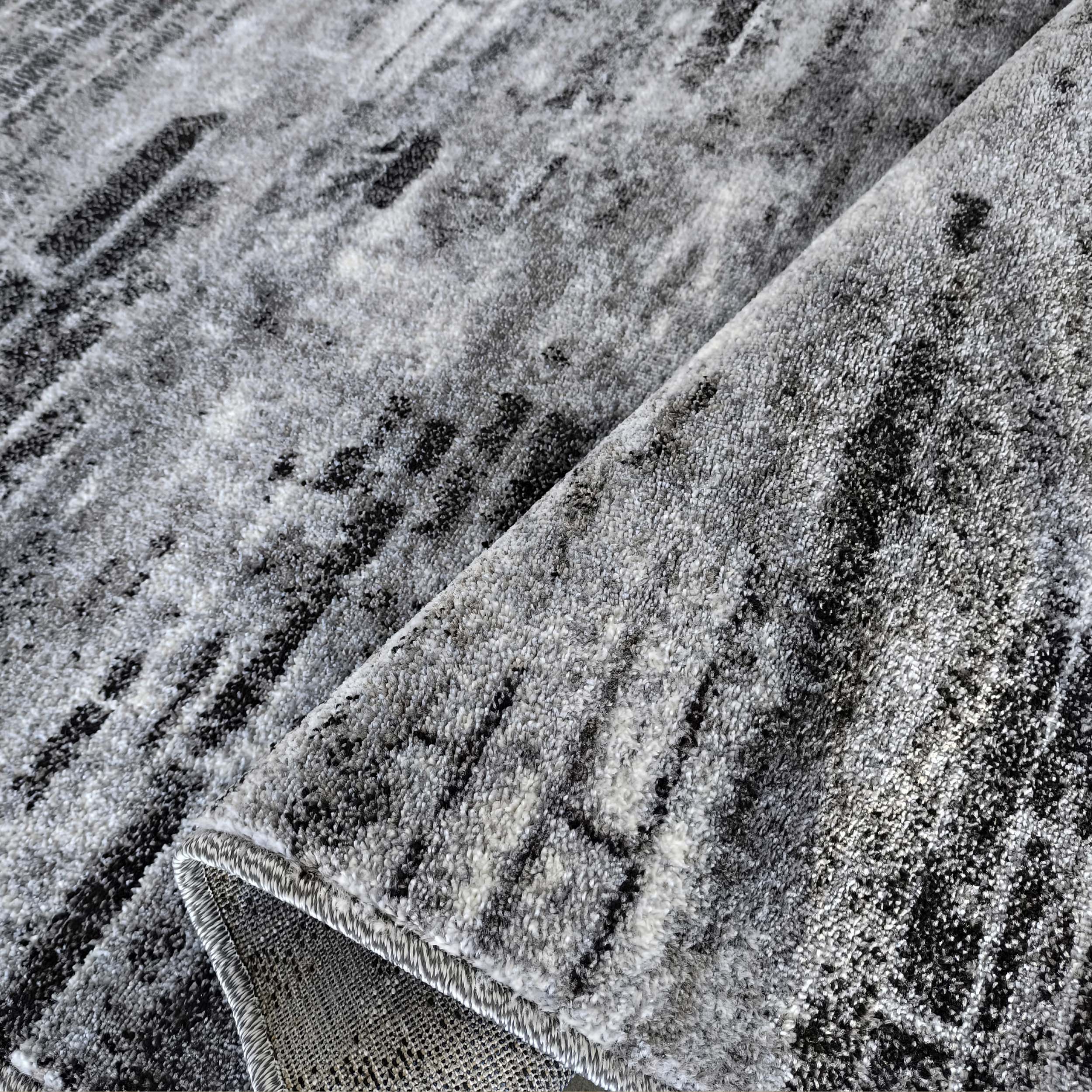 Tapis enroulé avec un motif abstrait de traits gris clairs, gris foncés et noirs, à texture douce et dense